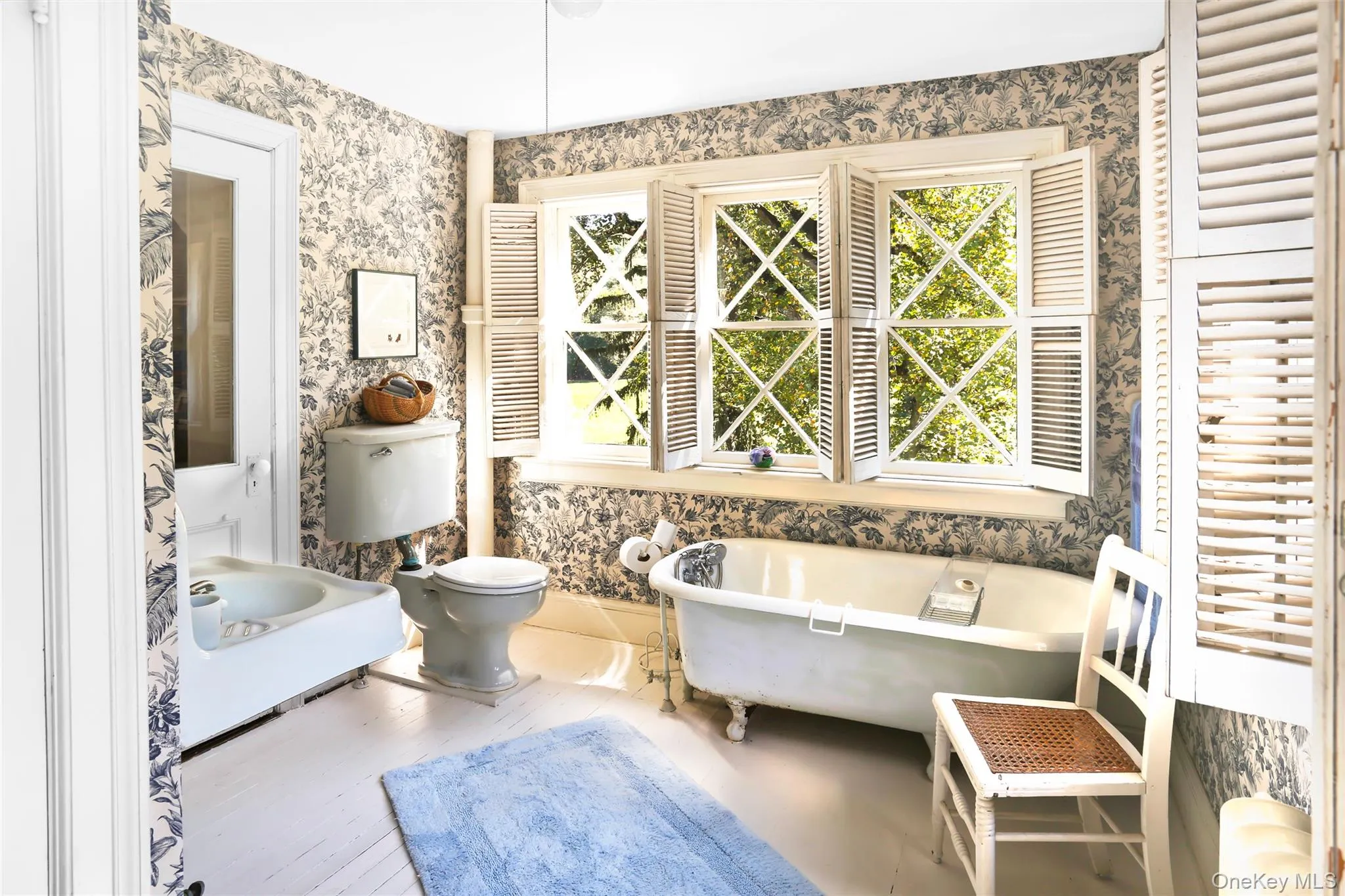 Bathroom featuring wallpapered walls, a freestanding bath, toilet, and wood finished floors Bathroom featuring wallpapered walls, a freestanding bath, toilet, and wood finished floors
