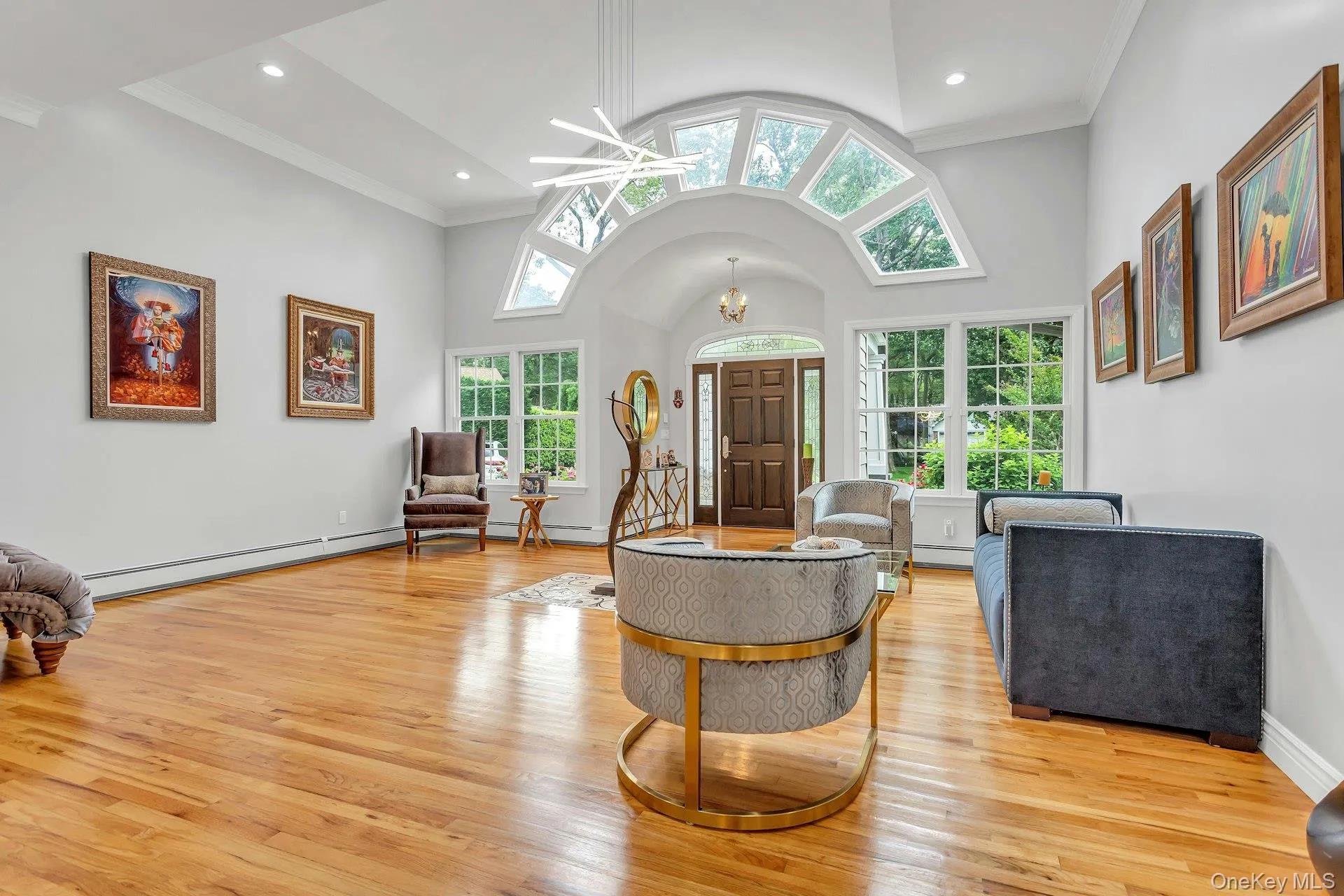 Entryway featuring light wood finished floors, baseboard heating, ornamental molding, a chandelier, and high vaulted ceiling Entryway featuring light wood finished floors, baseboard heating, ornamental molding, a chandelier, and high vaulted ceiling