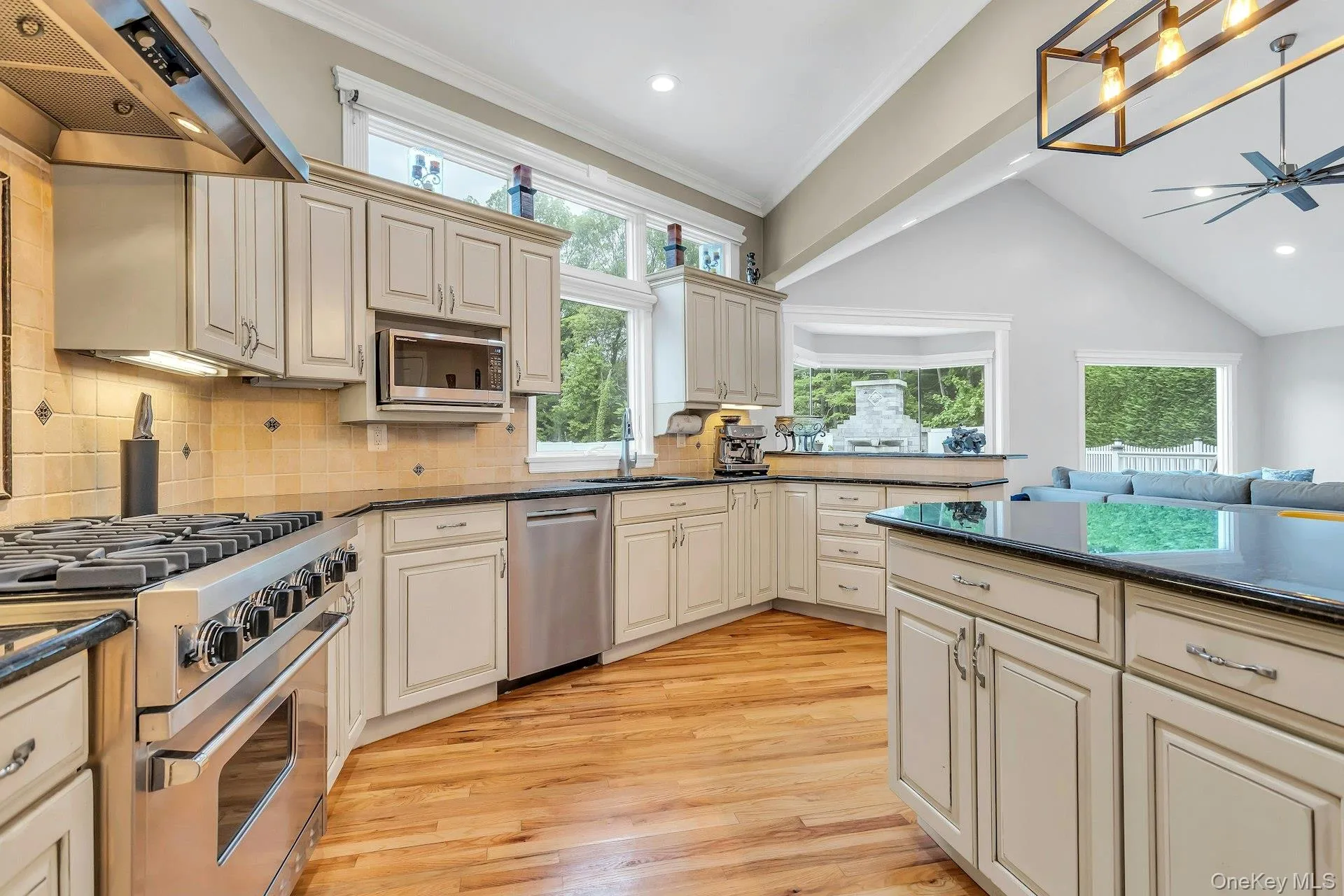 Kitchen with stainless steel appliances, range hood, light wood-style floors, dark countertops, and crown molding Kitchen with stainless steel appliances, range hood, light wood-style floors, dark countertops, and crown molding