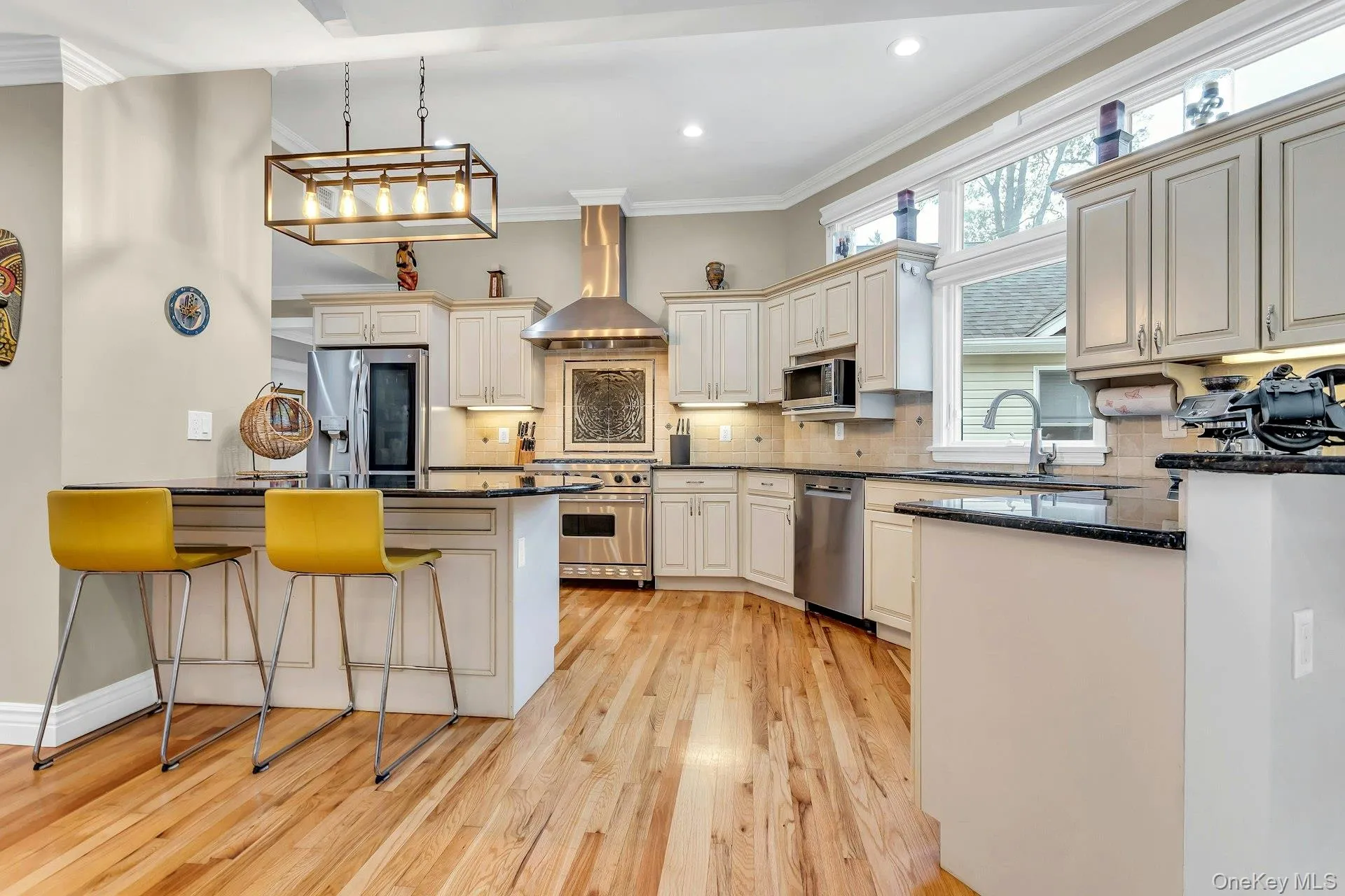 Kitchen featuring wall chimney exhaust hood, appliances with stainless steel finishes, a kitchen bar, light wood-type flooring, and a sink Kitchen featuring wall chimney exhaust hood, appliances with stainless steel finishes, a kitchen bar, light wood-type flooring, and a sink