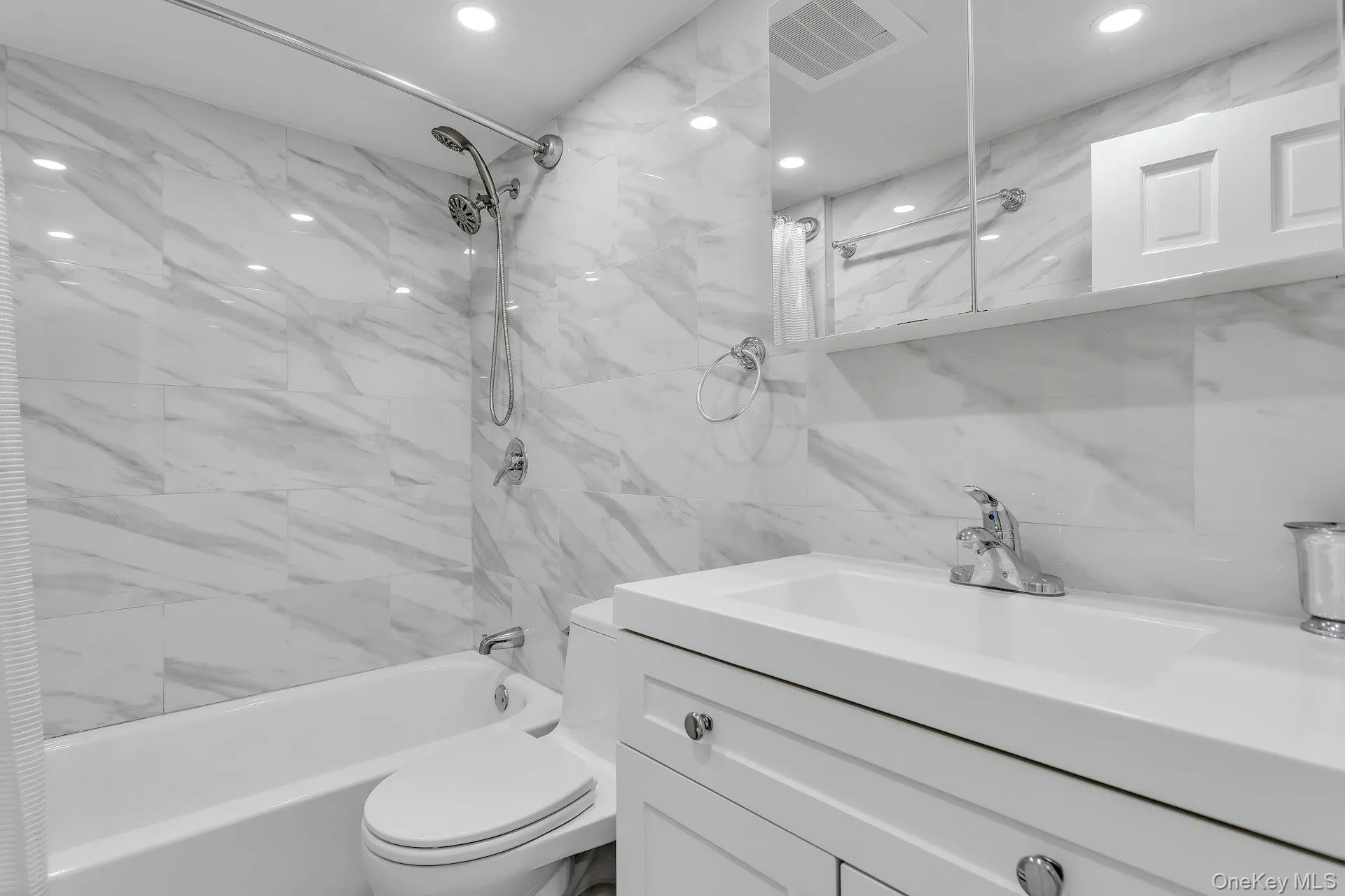 Full bathroom featuring vanity, shower combination, tile walls, toilet, and recessed lighting Full bathroom featuring vanity, shower combination, tile walls, toilet, and recessed lighting