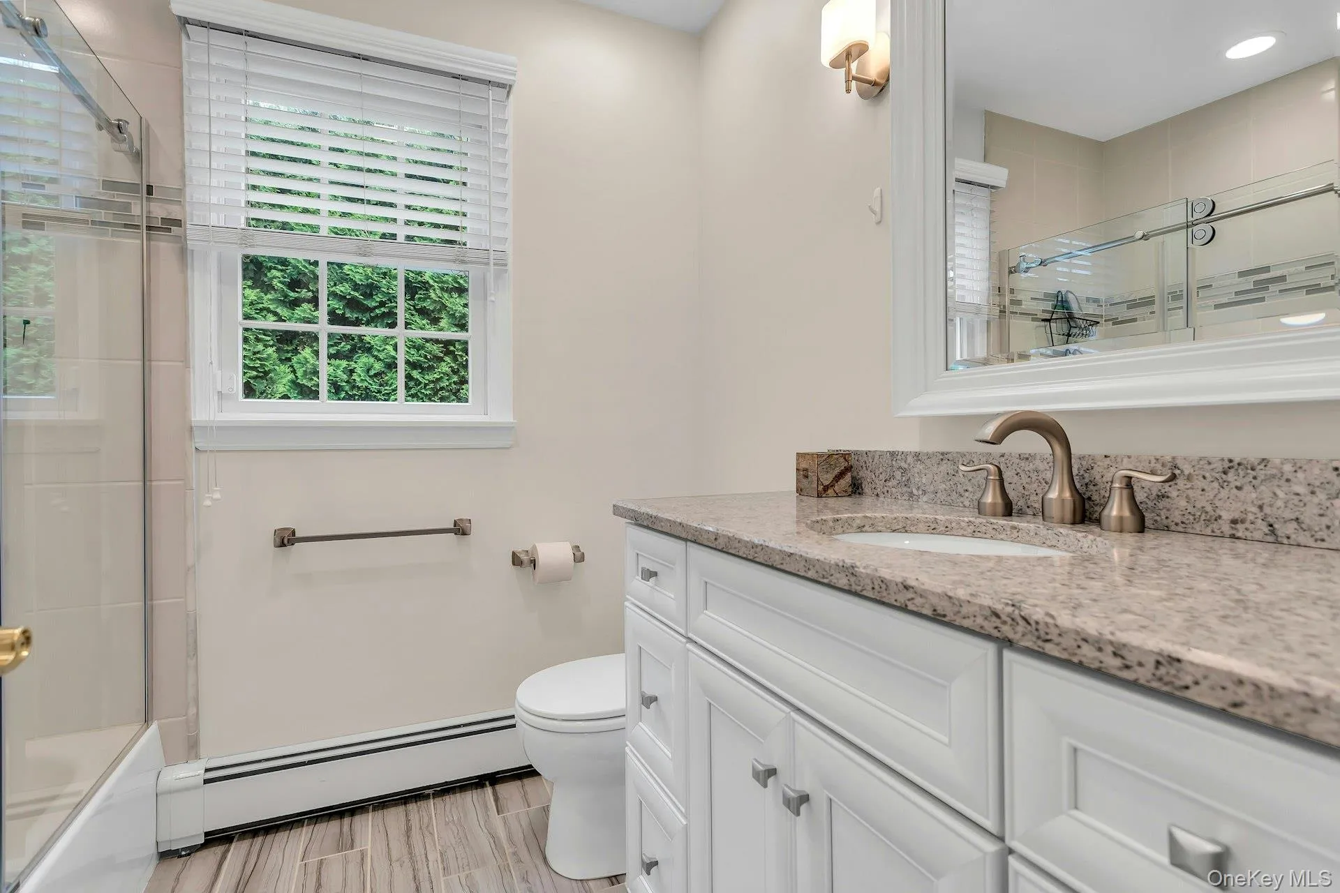 Bathroom featuring a baseboard heating unit, vanity, toilet, bath / shower combo with glass door, and wood finished floors Bathroom featuring a baseboard heating unit, vanity, toilet, bath / shower combo with glass door, and wood finished floors