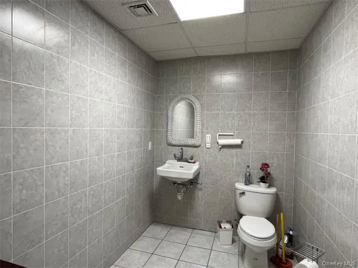 Half bathroom with tile walls, tile patterned floors, toilet, a sink, and a paneled ceiling Half bathroom with tile walls, tile patterned floors, toilet, a sink, and a paneled ceiling