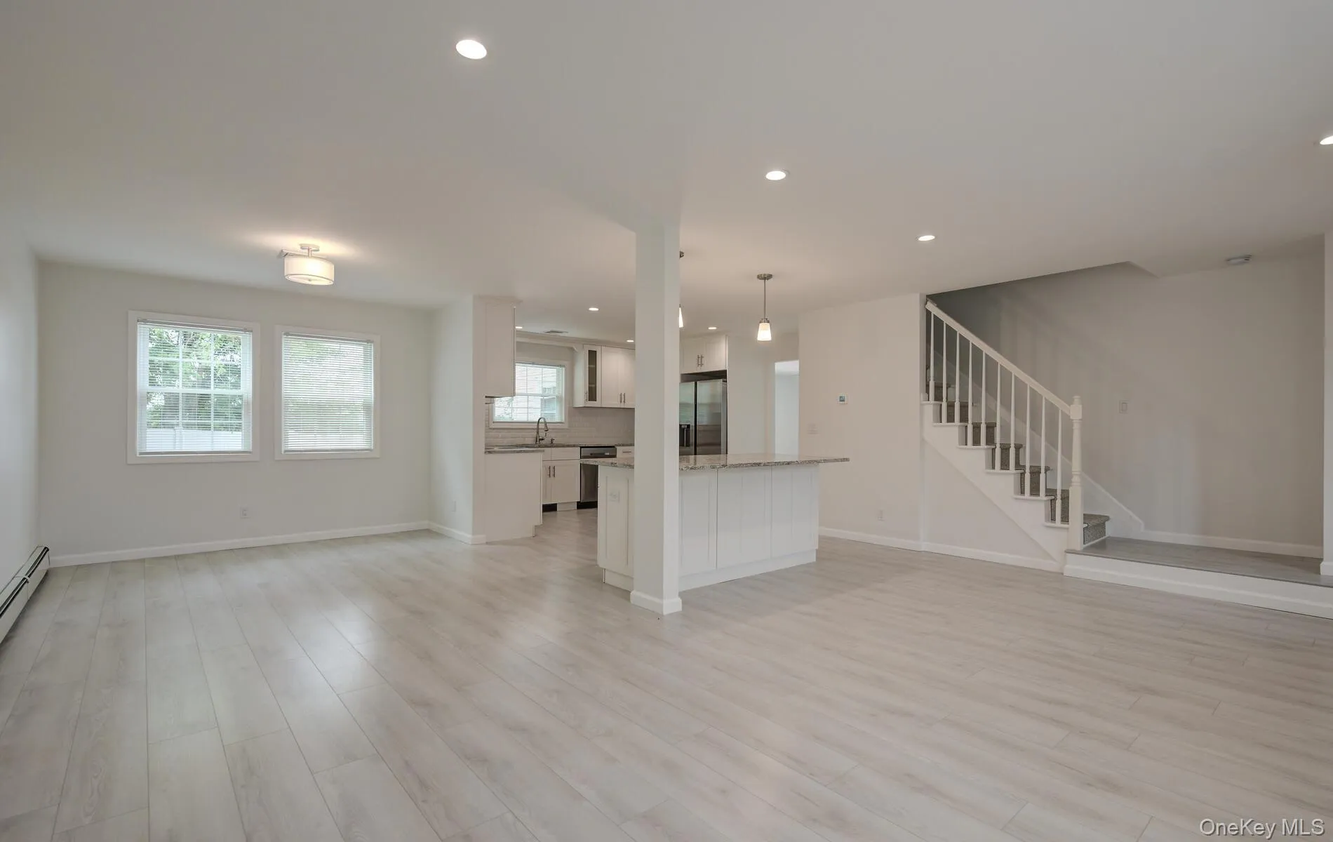 Unfurnished living room with a sink, light wood-style floors, healthy amount of natural light, recessed lighting, and stairway Unfurnished living room with a sink, light wood-style floors, healthy amount of natural light, recessed lighting, and stairway