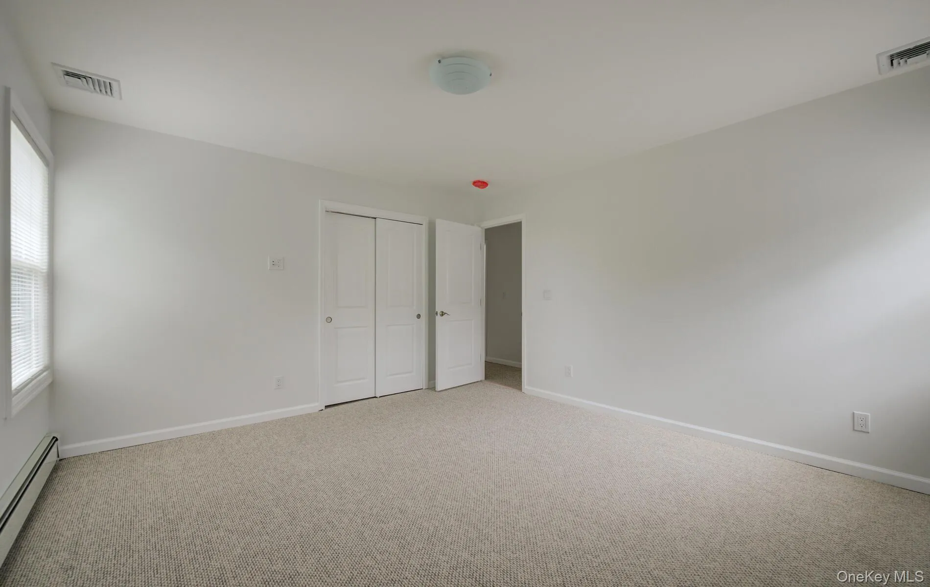 Unfurnished bedroom with a baseboard radiator, multiple windows, and light carpet Unfurnished bedroom with a baseboard radiator, multiple windows, and light carpet
