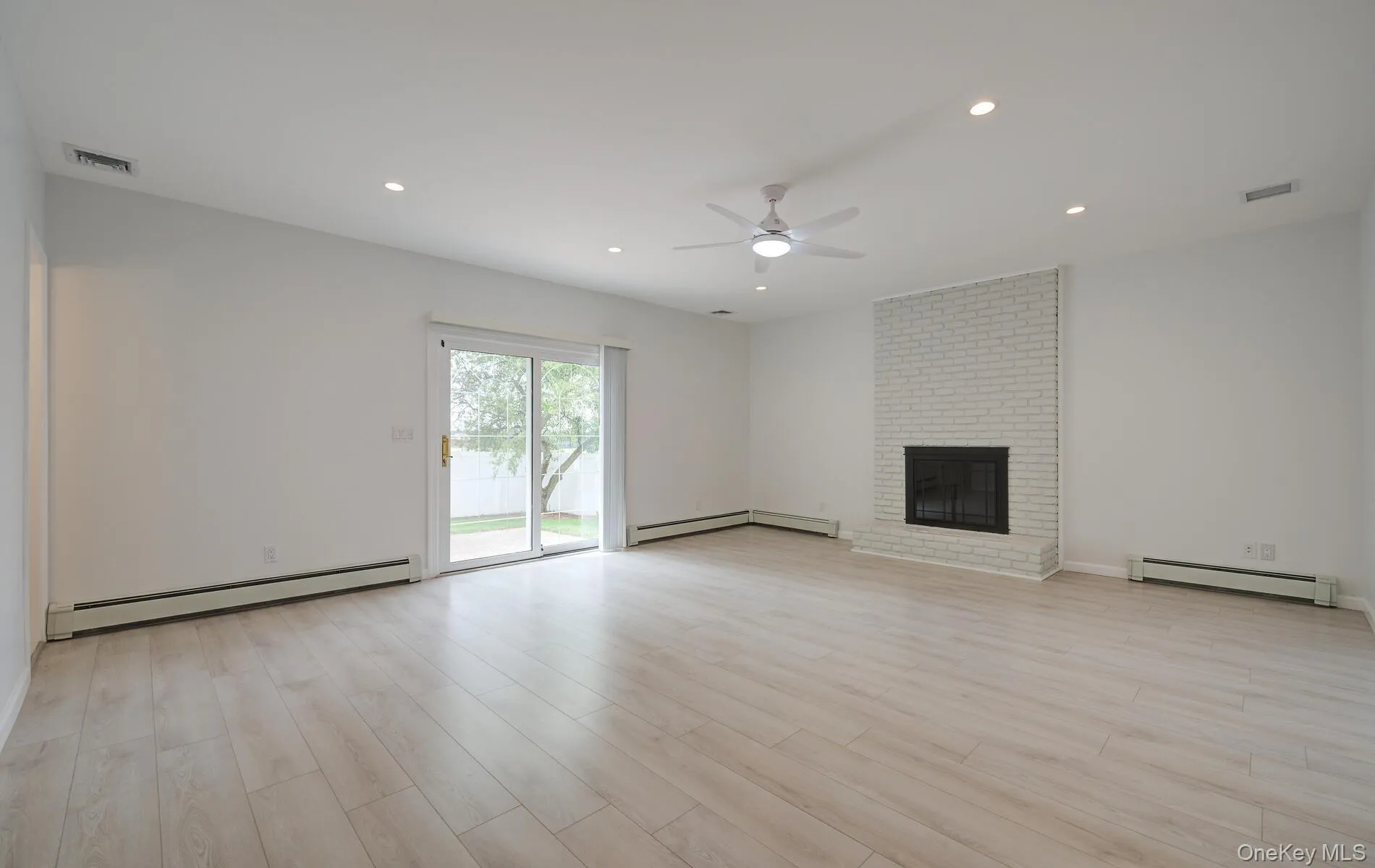 Unfurnished living room featuring a baseboard heating unit, a ceiling fan, light wood-style flooring, a brick fireplace, and recessed lighting Unfurnished living room featuring a baseboard heating unit, a ceiling fan, light wood-style flooring, a brick fireplace, and recessed lighting