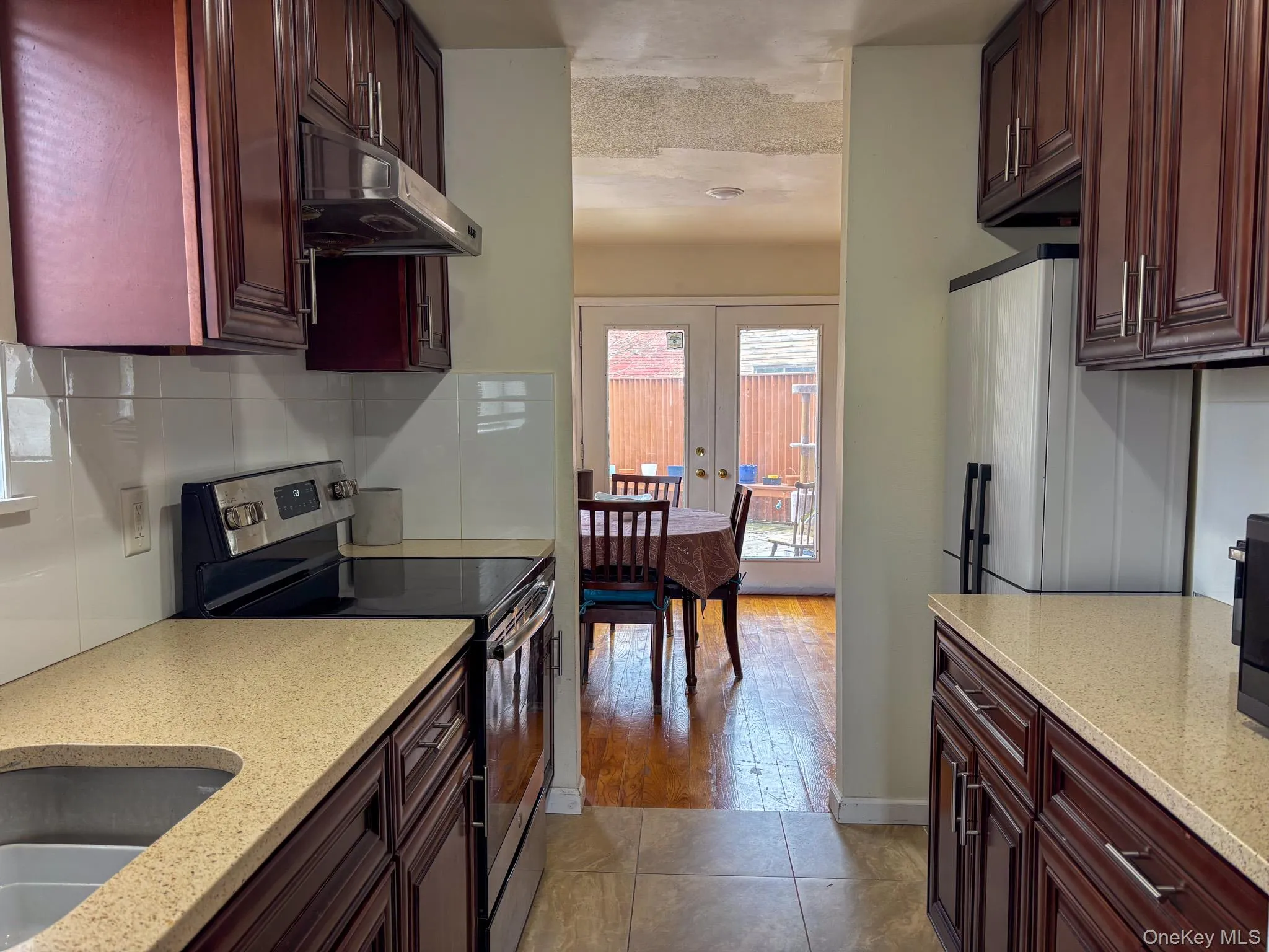Kitchen with electric stove, ventilation hood, tasteful backsplash, reddish brown cabinets, and a textured ceiling Kitchen with electric stove, ventilation hood, tasteful backsplash, reddish brown cabinets, and a textured ceiling