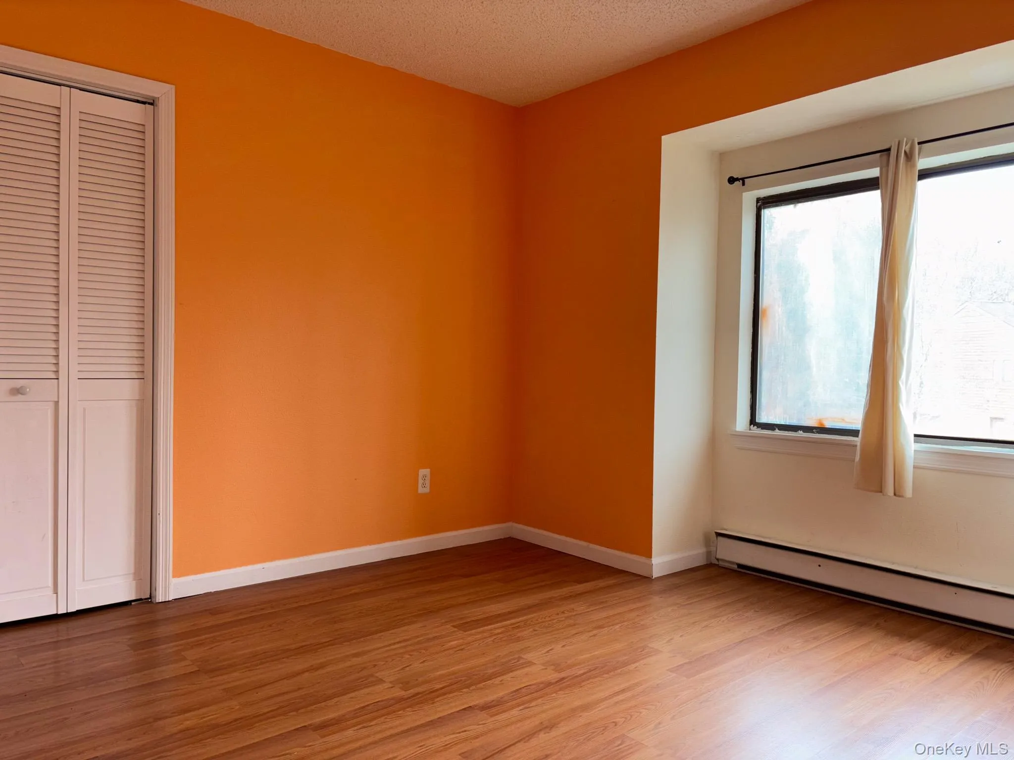 Unfurnished bedroom with light wood finished floors, baseboard heating, a closet, and a textured ceiling Unfurnished bedroom with light wood finished floors, baseboard heating, a closet, and a textured ceiling