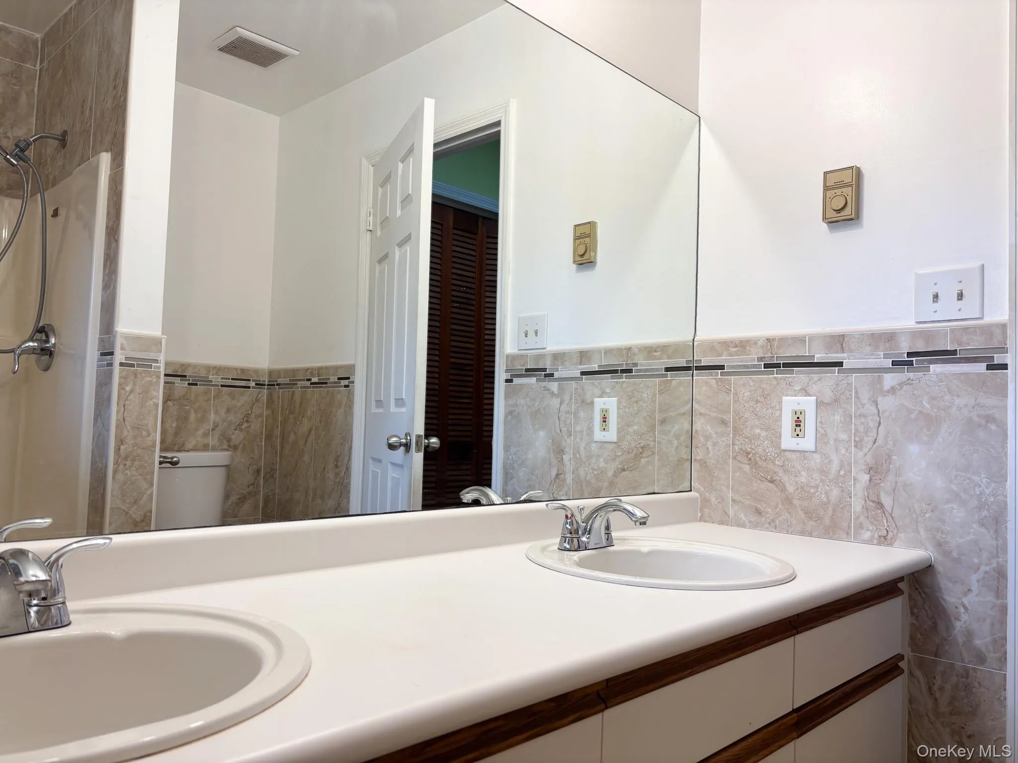 Primary full bathroom featuring double vanity, tile walls, wainscoting, and toilet Primary full bathroom featuring double vanity, tile walls, wainscoting, and toilet