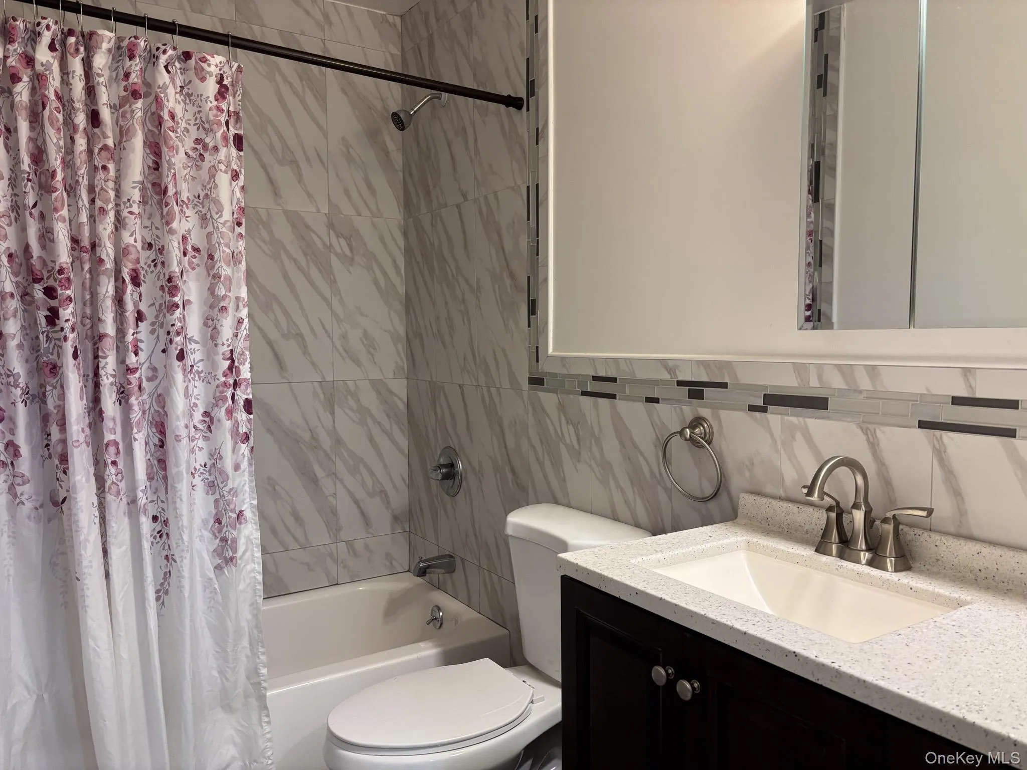 Full bathroom featuring toilet, shower / tub combo, vanity, and tasteful backsplash Full bathroom featuring toilet, shower / tub combo, vanity, and tasteful backsplash