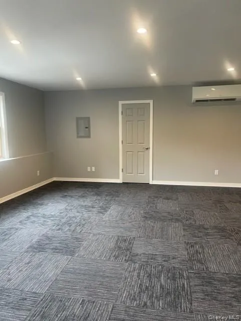 Unfurnished room with a wall mounted air conditioner, dark carpet, baseboards, recessed lighting, and electric panel Unfurnished room with a wall mounted air conditioner, dark carpet, baseboards, recessed lighting, and electric panel