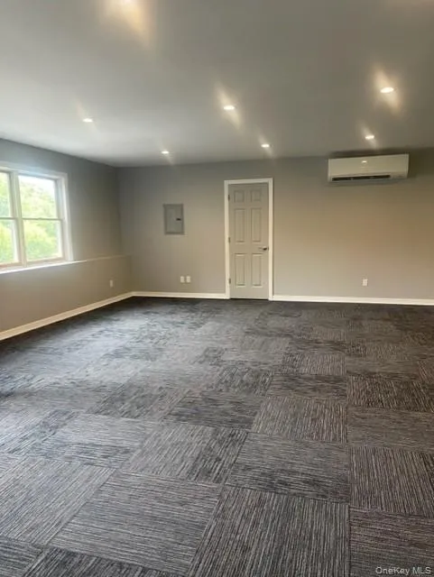 Spare room with an AC wall unit, dark colored carpet, electric panel, recessed lighting, and baseboards Spare room with an AC wall unit, dark colored carpet, electric panel, recessed lighting, and baseboards