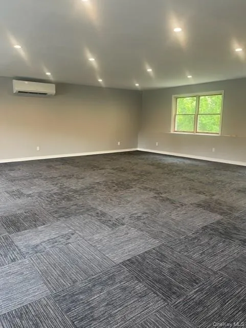 Empty room with a wall mounted air conditioner, dark colored carpet, baseboards, and recessed lighting Empty room with a wall mounted air conditioner, dark colored carpet, baseboards, and recessed lighting