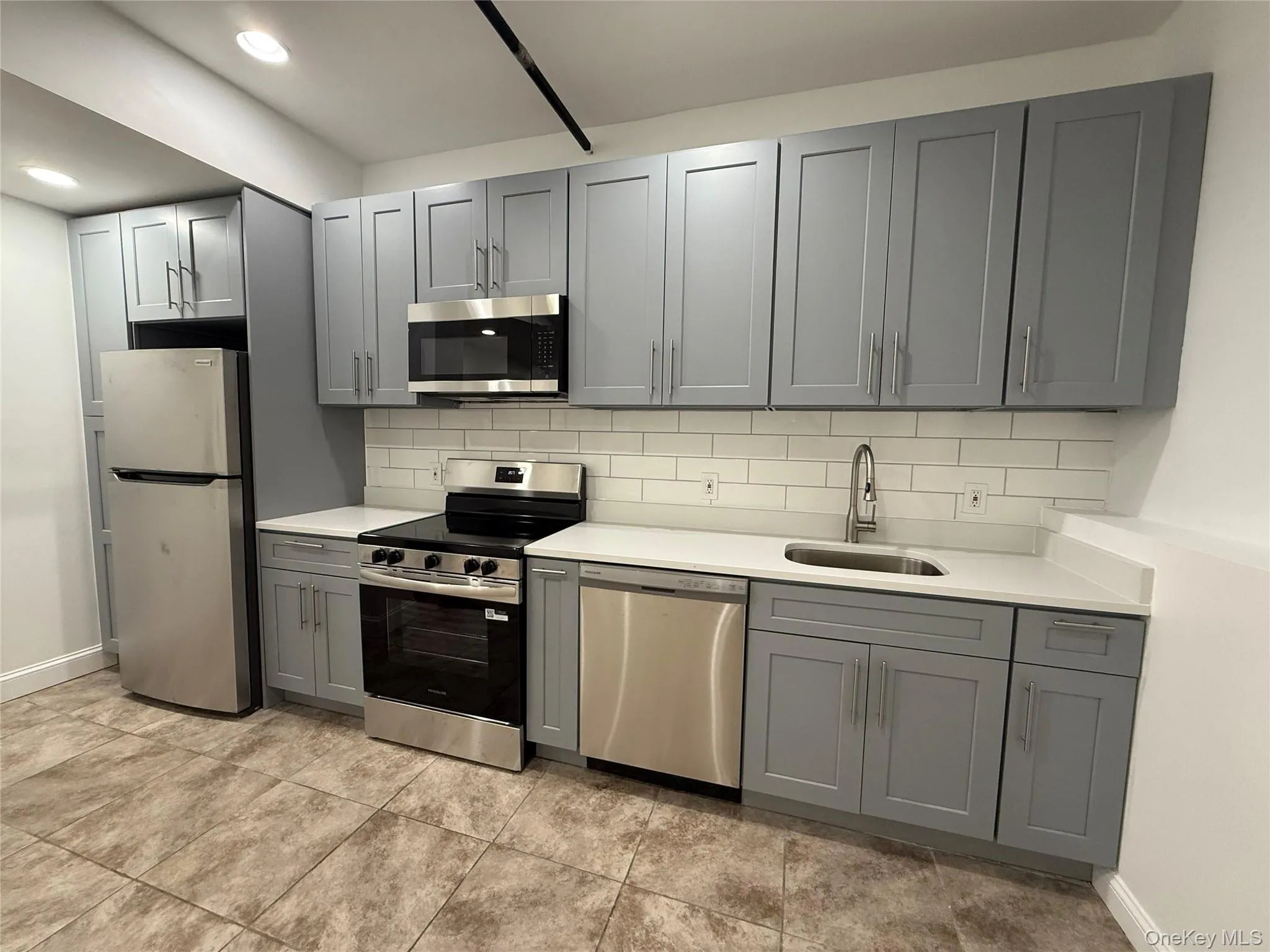 Kitchen with stainless steel appliances, gray cabinetry, backsplash, light countertops, and recessed lighting Kitchen with stainless steel appliances, gray cabinetry, backsplash, light countertops, and recessed lighting