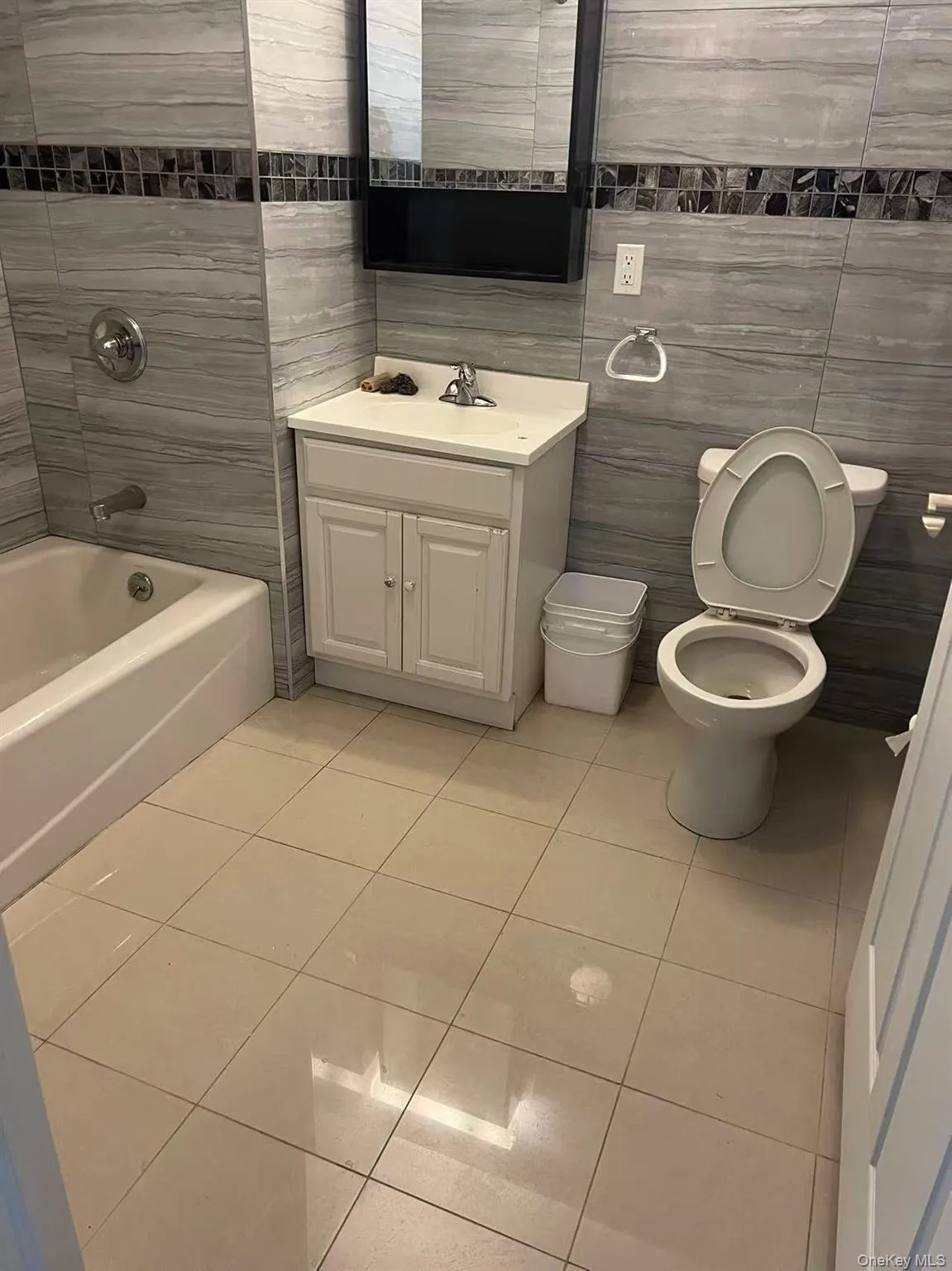 Bathroom featuring tile patterned flooring, toilet, vanity, tile walls, and washtub / shower combination Bathroom featuring tile patterned flooring, toilet, vanity, tile walls, and washtub / shower combination