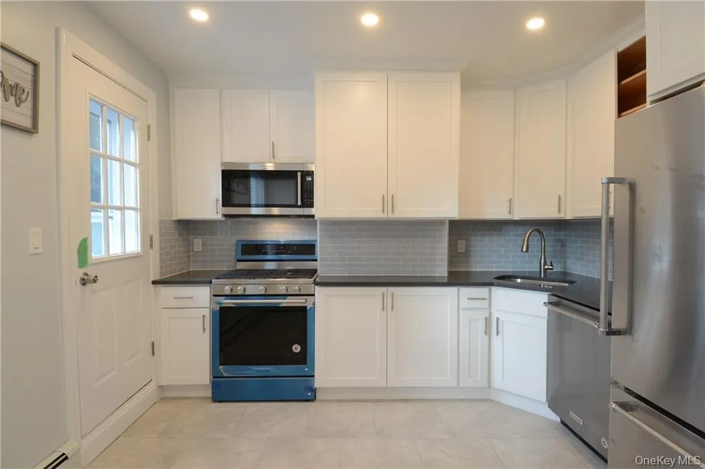 Kitchen with stainless steel appliances, a sink, a baseboard heating unit, white cabinets, and backsplash Kitchen with stainless steel appliances, a sink, a baseboard heating unit, white cabinets, and backsplash