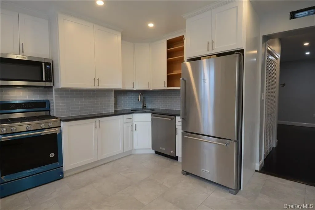 Kitchen with appliances with stainless steel finishes, open shelves, a sink, decorative backsplash, and dark countertops Kitchen with appliances with stainless steel finishes, open shelves, a sink, decorative backsplash, and dark countertops