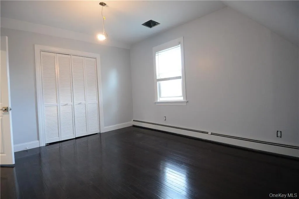 Unfurnished bedroom with baseboard heating, dark wood finished floors, baseboards, lofted ceiling, and a closet Unfurnished bedroom with baseboard heating, dark wood finished floors, baseboards, lofted ceiling, and a closet