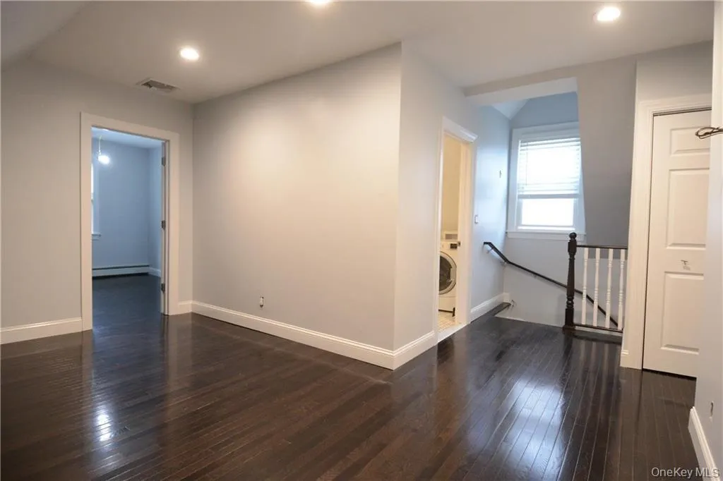 Empty room with a baseboard heating unit, washer / dryer, dark wood-style floors, recessed lighting, and baseboards Empty room with a baseboard heating unit, washer / dryer, dark wood-style floors, recessed lighting, and baseboards