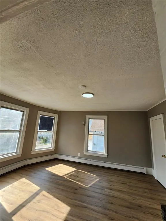 Spare room with dark wood finished floors, plenty of natural light, a textured ceiling, and baseboards Spare room with dark wood finished floors, plenty of natural light, a textured ceiling, and baseboards