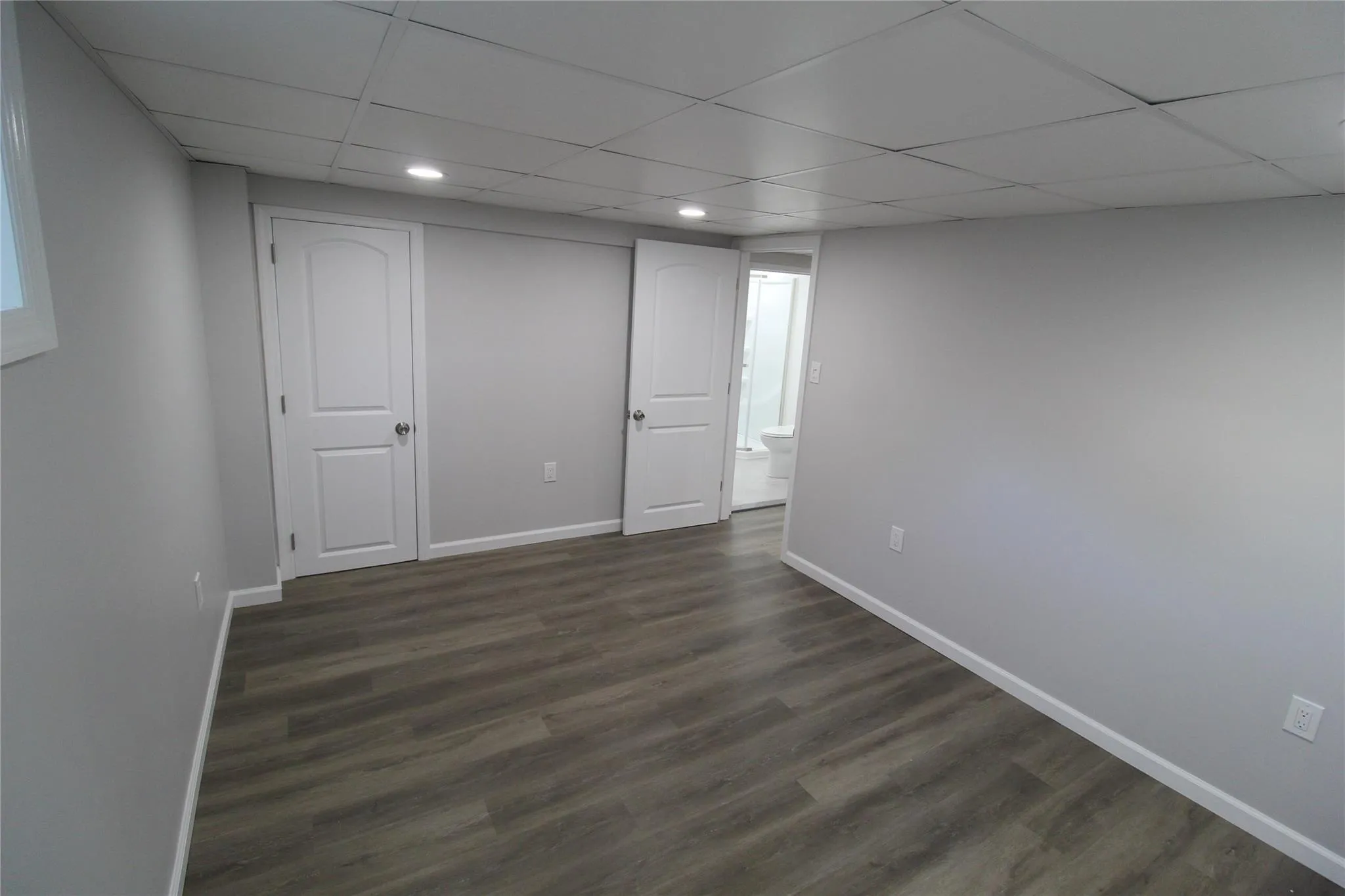Finished below grade area with dark wood-style floors, baseboards, a drop ceiling, and recessed lighting Finished below grade area with dark wood-style floors, baseboards, a drop ceiling, and recessed lighting