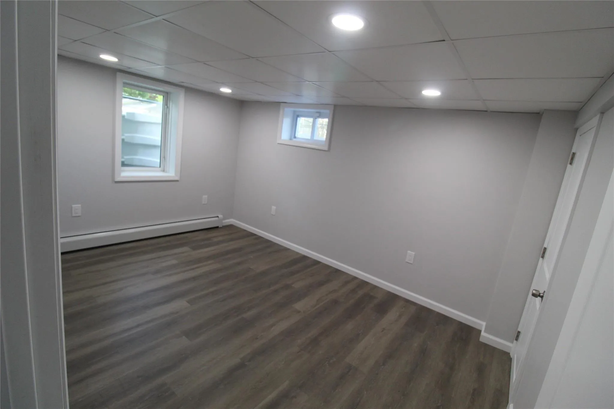 Below grade area with a baseboard heating unit, dark wood-type flooring, baseboards, recessed lighting, and a paneled ceiling Below grade area with a baseboard heating unit, dark wood-type flooring, baseboards, recessed lighting, and a paneled ceiling