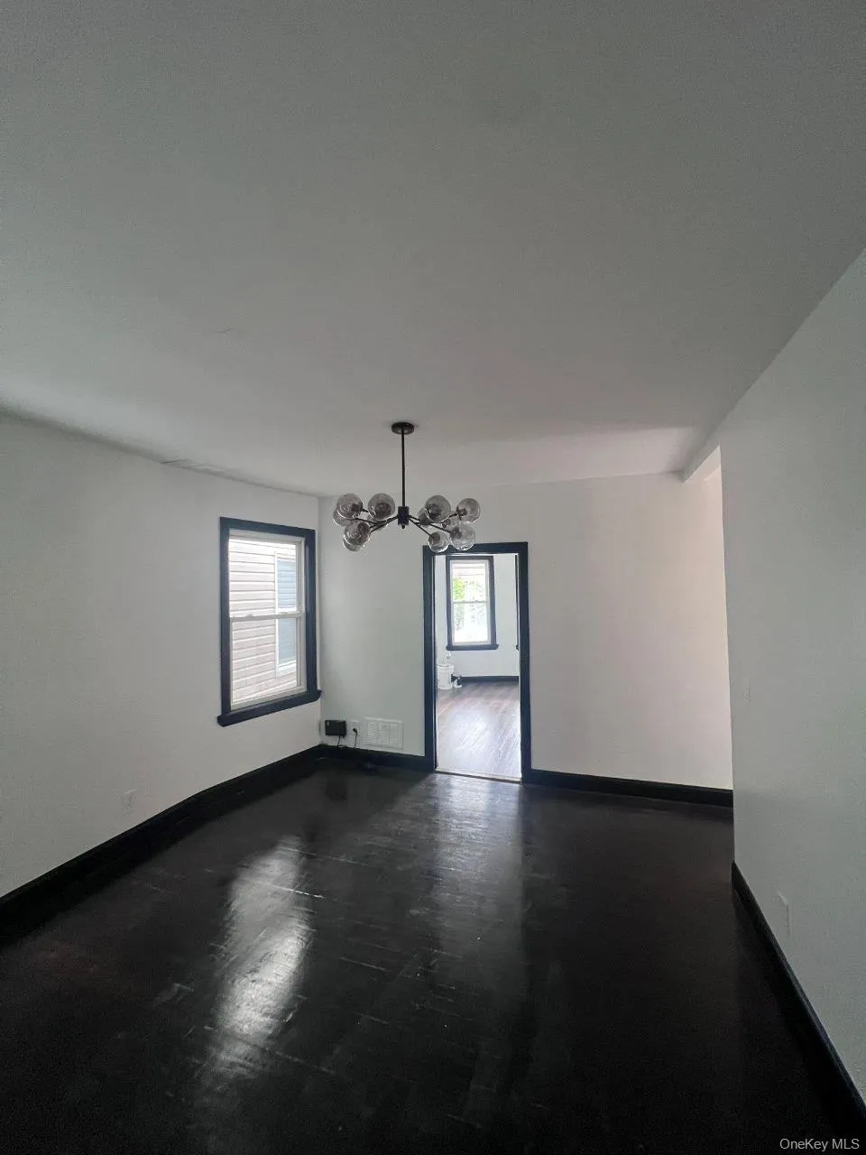 Empty room with a chandelier and dark wood-style floors Empty room with a chandelier and dark wood-style floors