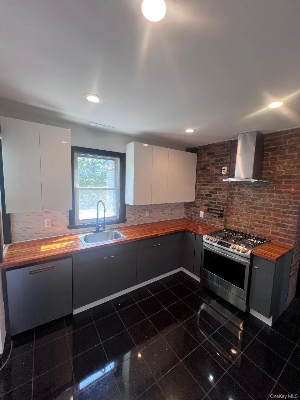 Kitchen featuring appliances with stainless steel finishes, wall chimney exhaust hood, white cabinetry, granite floors, and decorative backsplash Kitchen featuring appliances with stainless steel finishes, wall chimney exhaust hood, white cabinetry, granite floors, and decorative backsplash