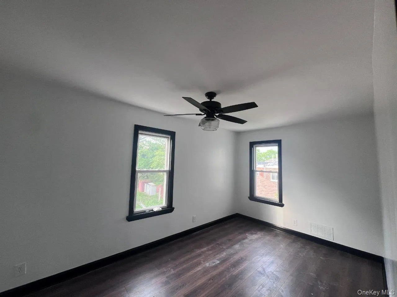 Empty room with healthy amount of natural light, dark wood-type flooring, and a ceiling fan Empty room with healthy amount of natural light, dark wood-type flooring, and a ceiling fan