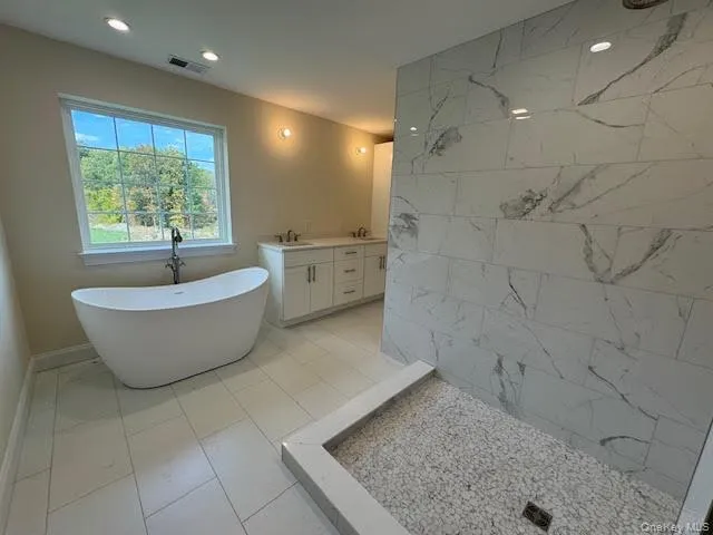 Bathroom featuring a marble finish shower, double vanity, a freestanding tub, recessed lighting, and light tile patterned flooring Bathroom featuring a marble finish shower, double vanity, a freestanding tub, recessed lighting, and light tile patterned flooring