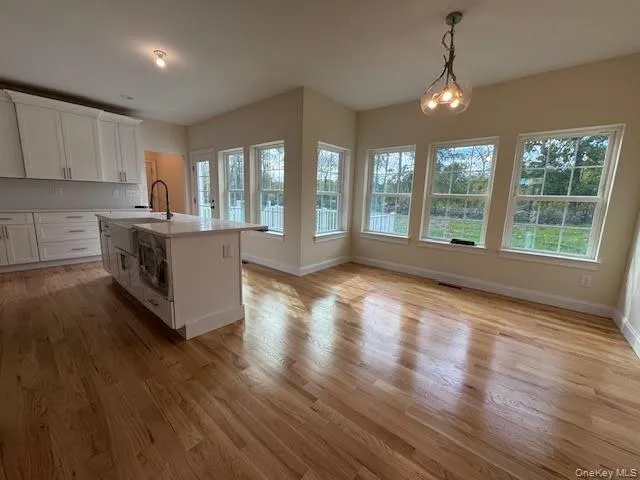 Kitchen with a kitchen island with sink, white cabinetry, hanging light fixtures, and light wood finished floors Kitchen with a kitchen island with sink, white cabinetry, hanging light fixtures, and light wood finished floors