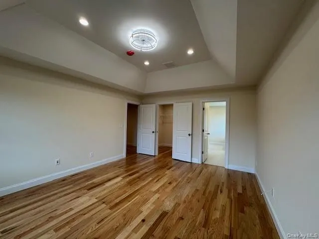 Unfurnished bedroom featuring a walk in closet, a raised ceiling, light wood-style floors, and recessed lighting Unfurnished bedroom featuring a walk in closet, a raised ceiling, light wood-style floors, and recessed lighting
