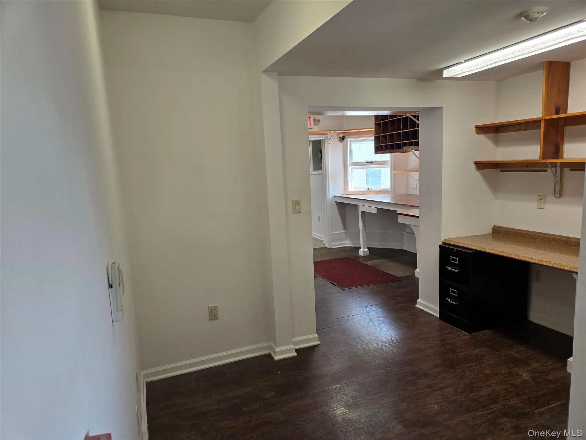 Unfurnished office with built in study area, baseboards, and dark wood-style flooring Unfurnished office with built in study area, baseboards, and dark wood-style flooring