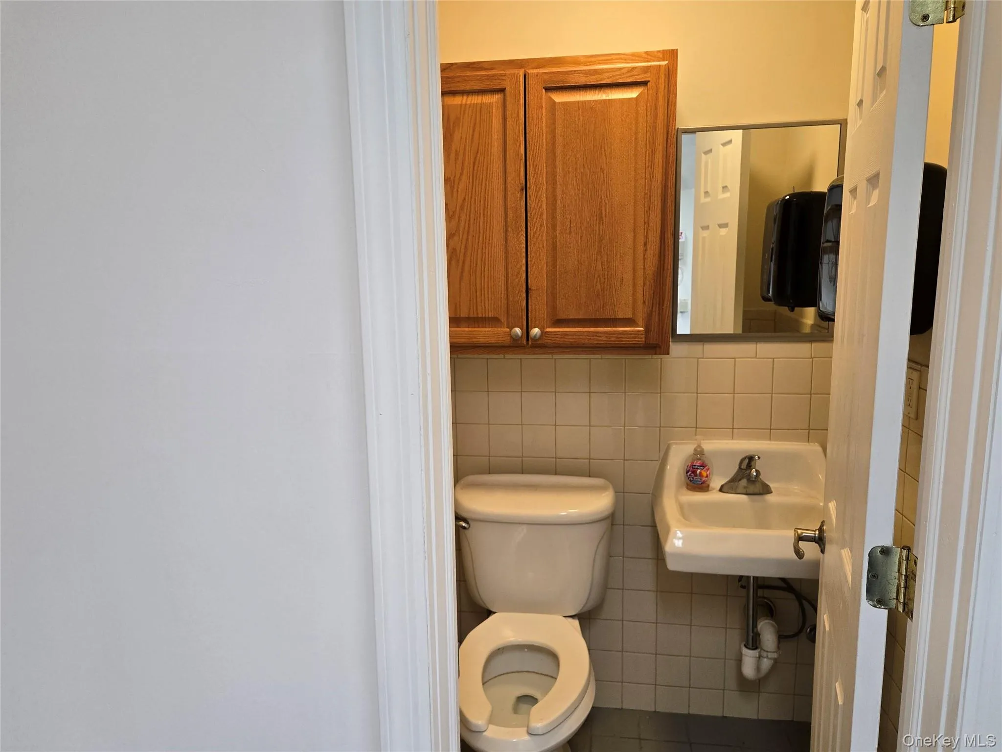 Bathroom with toilet, tile walls, a sink, and tile patterned flooring Bathroom with toilet, tile walls, a sink, and tile patterned flooring