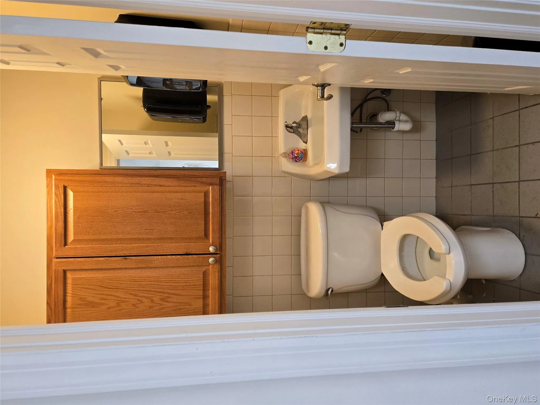 Bathroom with toilet, tile patterned flooring, tile walls, and a sink Bathroom with toilet, tile patterned flooring, tile walls, and a sink