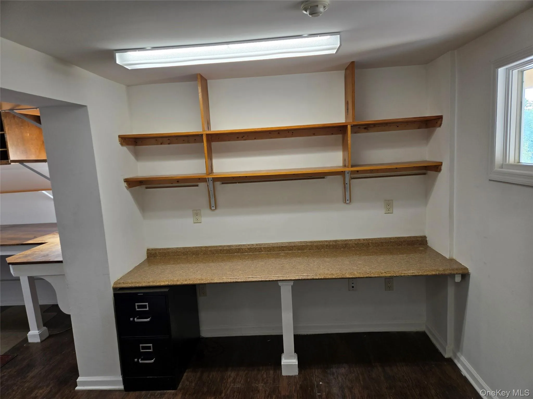 Unfurnished office with dark wood-type flooring, built in desk, and baseboards Unfurnished office with dark wood-type flooring, built in desk, and baseboards