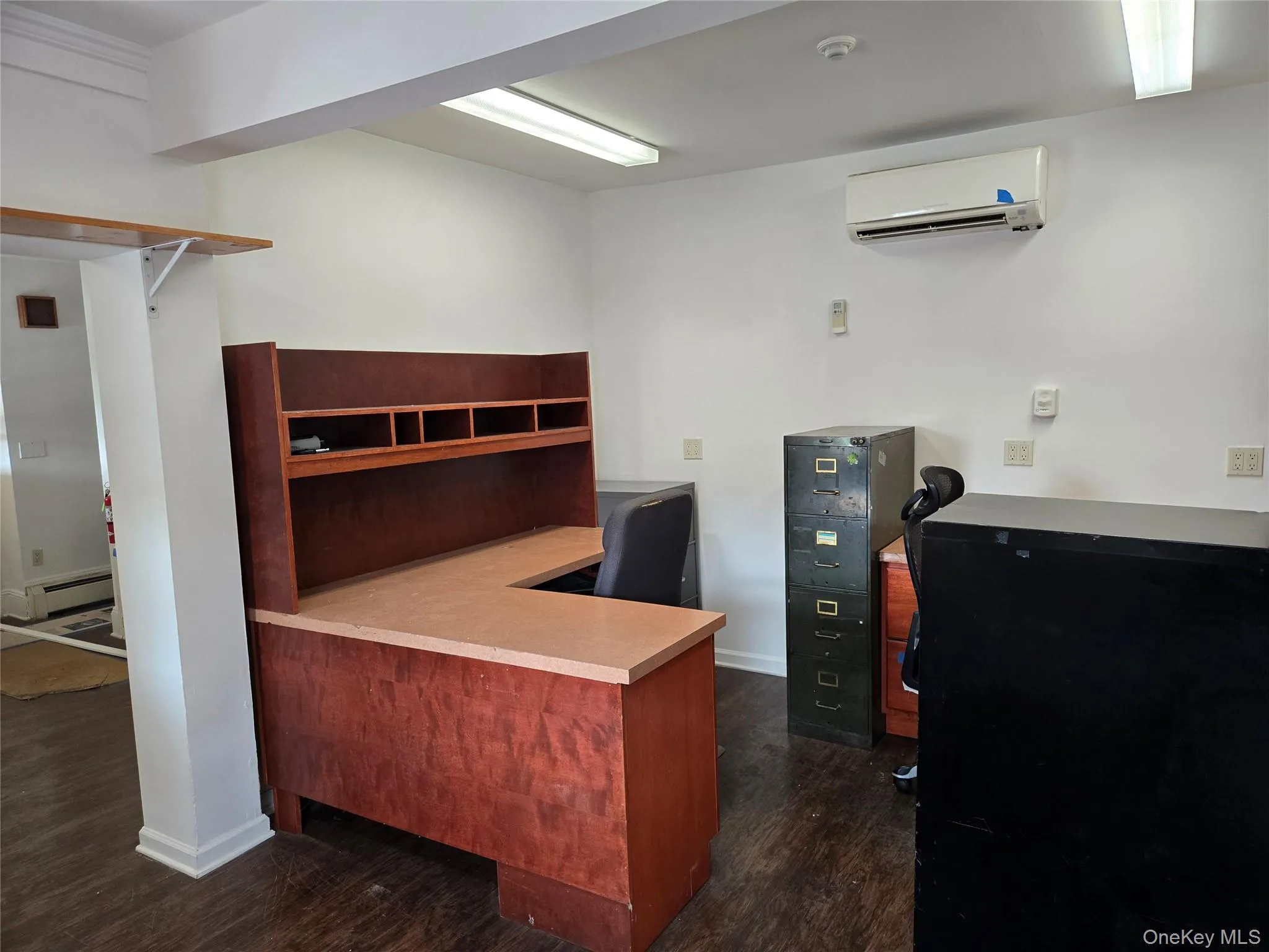 Office space featuring an AC wall unit, dark wood-style flooring, and a baseboard heating unit Office space featuring an AC wall unit, dark wood-style flooring, and a baseboard heating unit