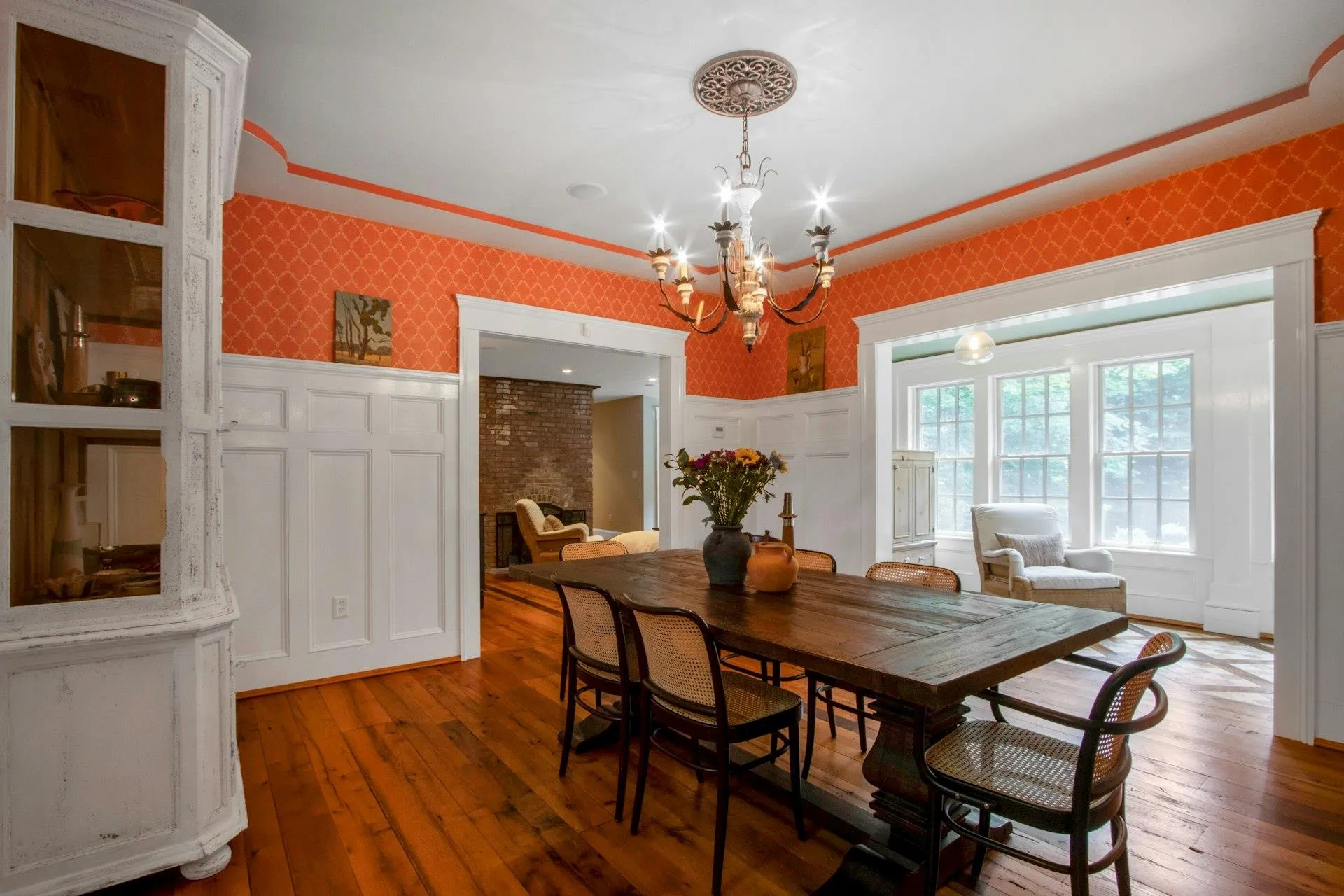 Dining space with wallpapered walls, a chandelier, wood-type flooring, a wainscoted wall, and a decorative wall Dining space with wallpapered walls, a chandelier, wood-type flooring, a wainscoted wall, and a decorative wall