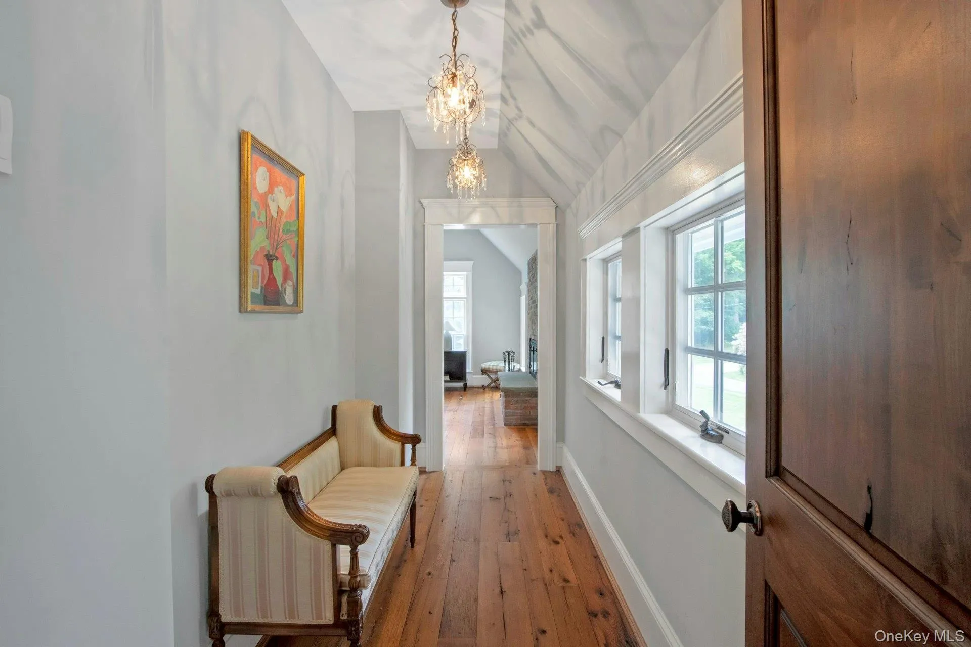 Corridor featuring a chandelier, vaulted ceiling, light wood-type flooring, and baseboards Corridor featuring a chandelier, vaulted ceiling, light wood-type flooring, and baseboards