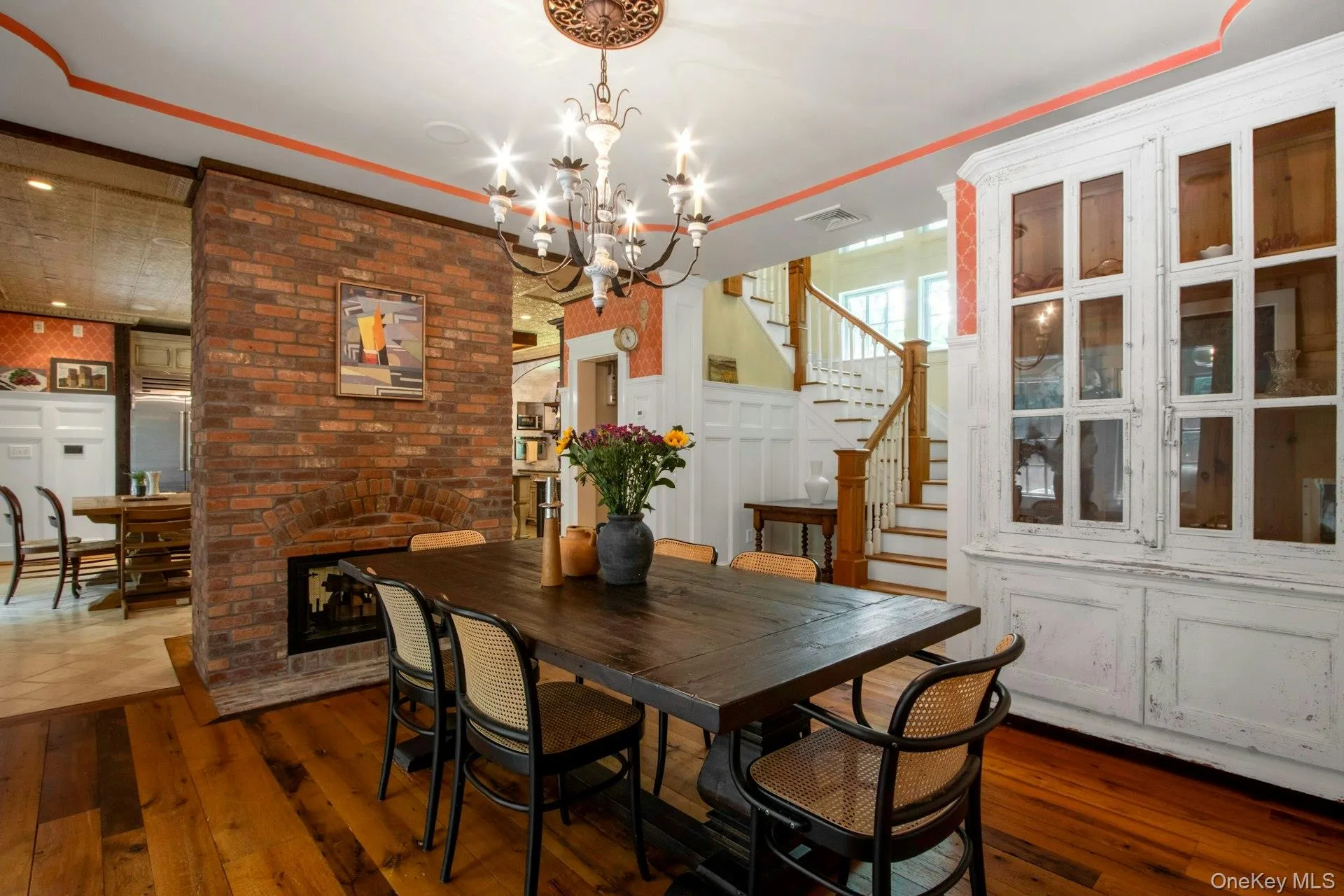 Dining room with dark wood-style floors, a chandelier, stairs, and a fireplace Dining room with dark wood-style floors, a chandelier, stairs, and a fireplace