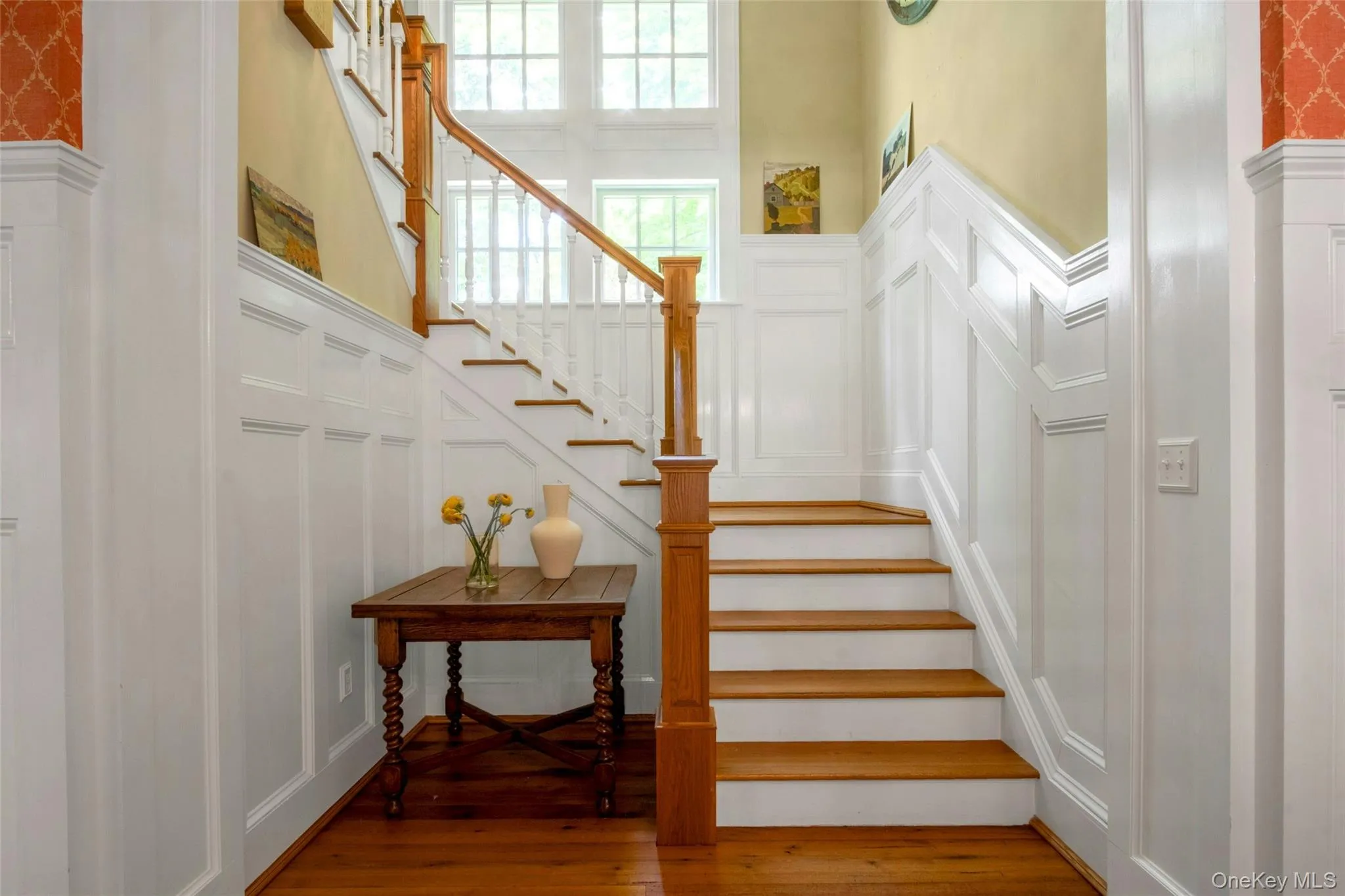 Stairs featuring a decorative wall, hardwood / wood-style flooring, wainscoting, and a towering ceiling Stairs featuring a decorative wall, hardwood / wood-style flooring, wainscoting, and a towering ceiling