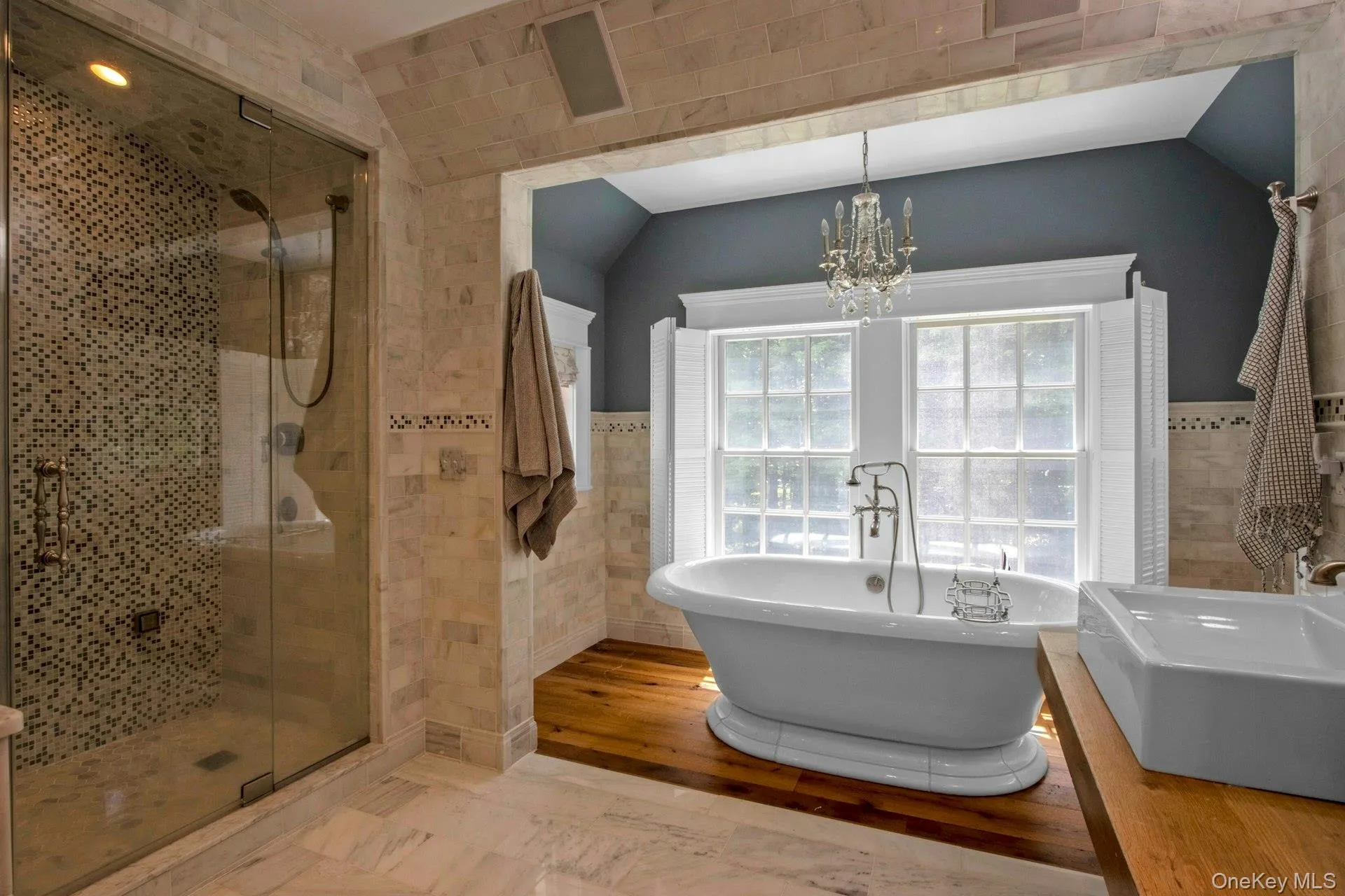 Full bathroom featuring tile walls, a soaking tub, a chandelier, a shower stall, and wainscoting Full bathroom featuring tile walls, a soaking tub, a chandelier, a shower stall, and wainscoting