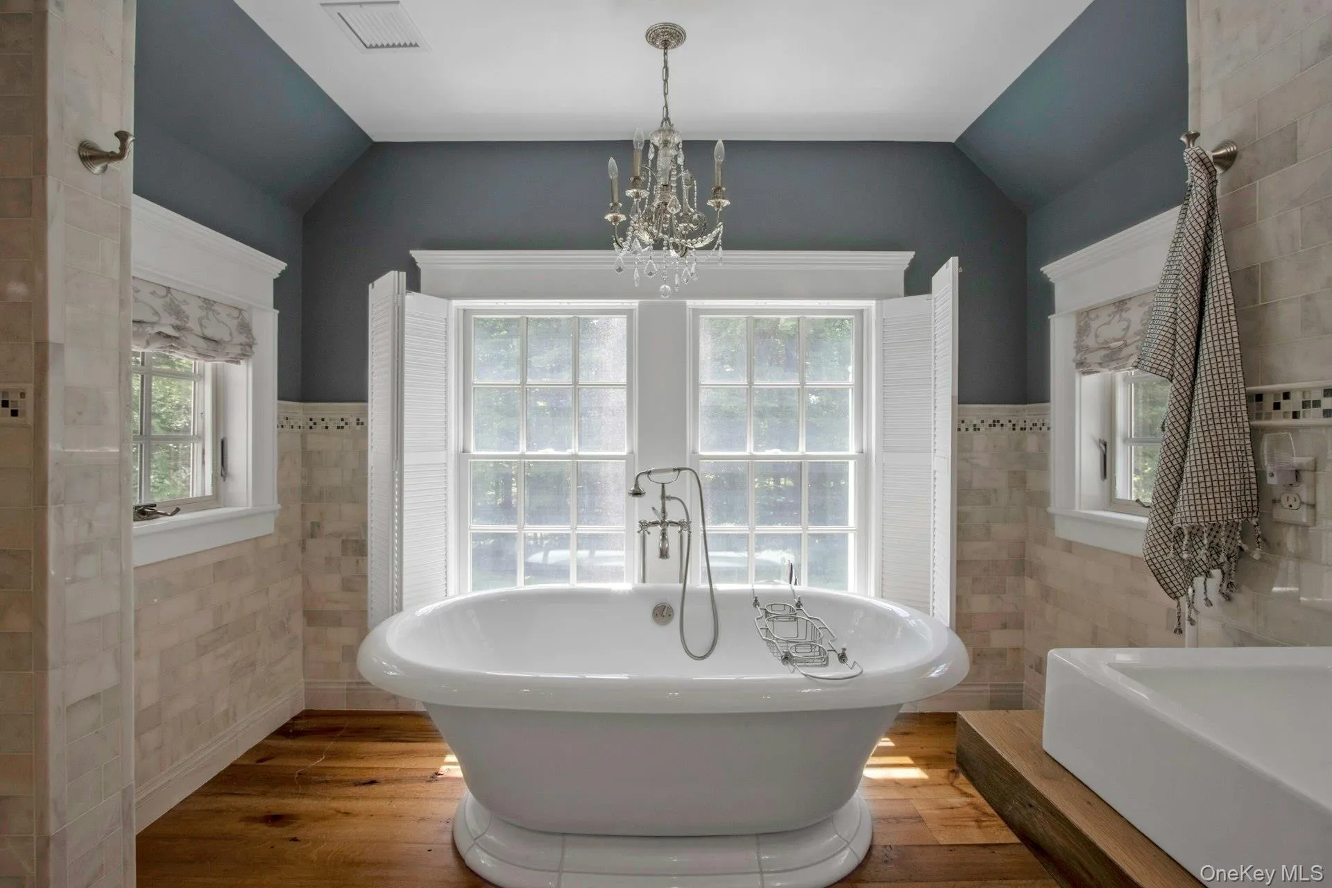 Bathroom featuring tile walls, vaulted ceiling, a chandelier, a soaking tub, and wood finished floors Bathroom featuring tile walls, vaulted ceiling, a chandelier, a soaking tub, and wood finished floors