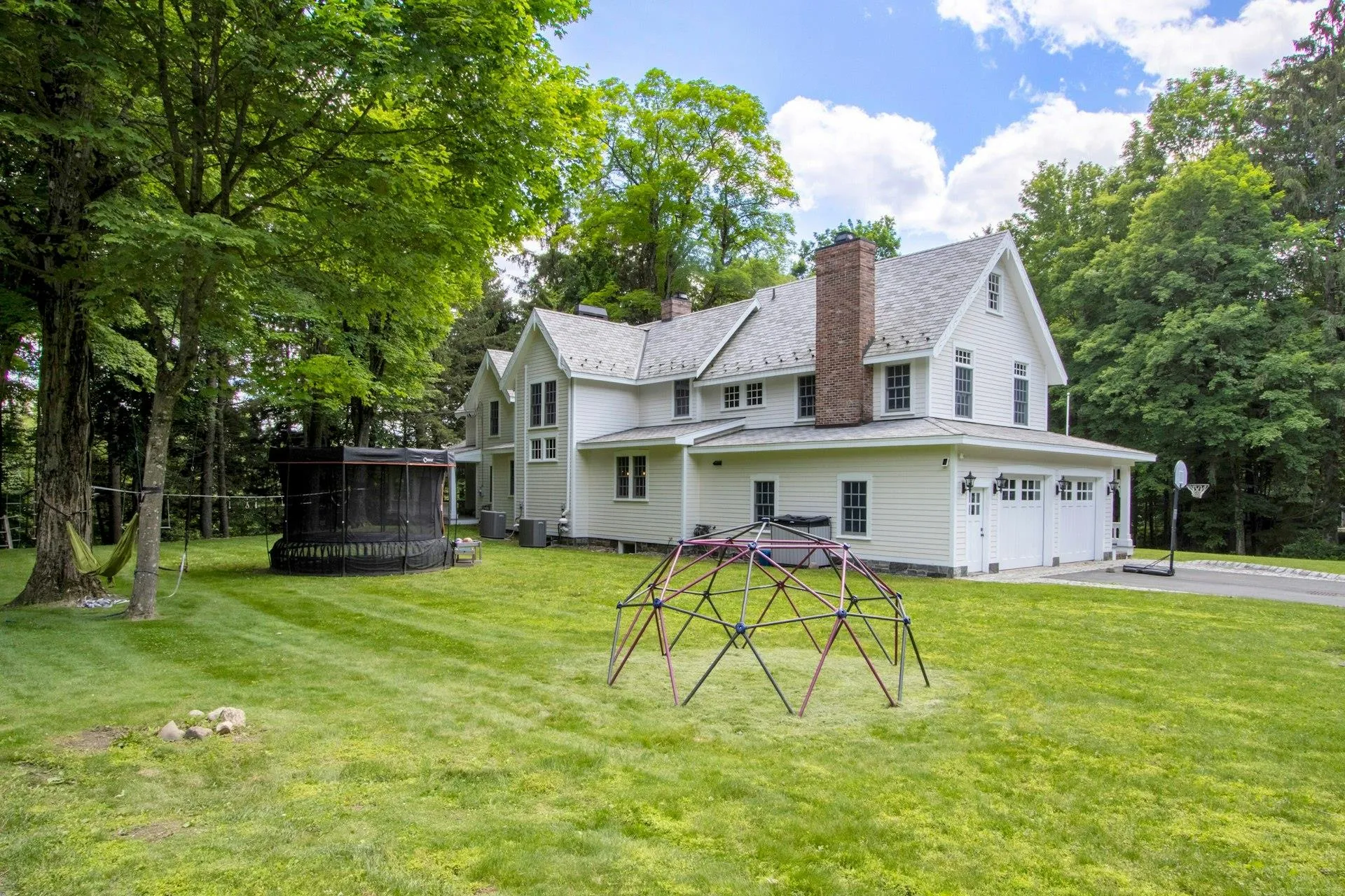 Back of house featuring a chimney, an attached garage, a lawn, central AC unit, and asphalt driveway Back of house featuring a chimney, an attached garage, a lawn, central AC unit, and asphalt driveway