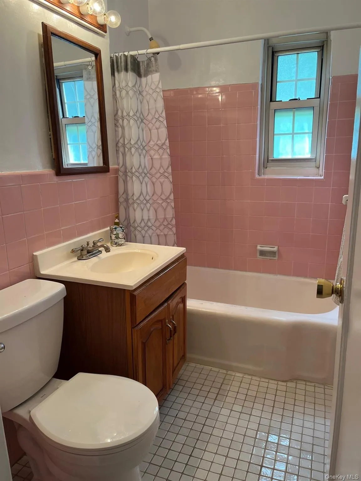 Bathroom with tile walls, tile patterned floors, toilet, vanity, and shower / bathtub combination with curtain Bathroom with tile walls, tile patterned floors, toilet, vanity, and shower / bathtub combination with curtain