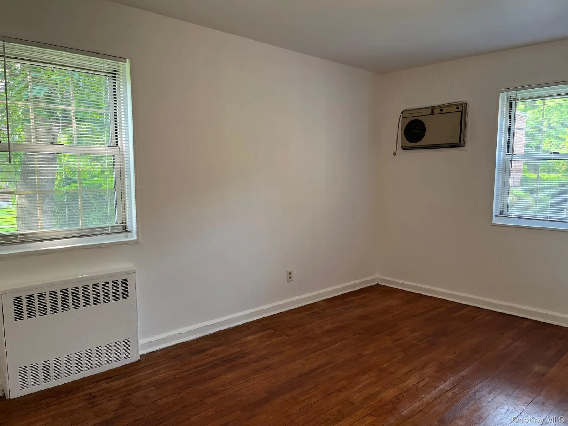Bedroom with hardwood flooring, wall A/C, radiator for heating Bedroom with hardwood flooring, wall A/C, radiator for heating