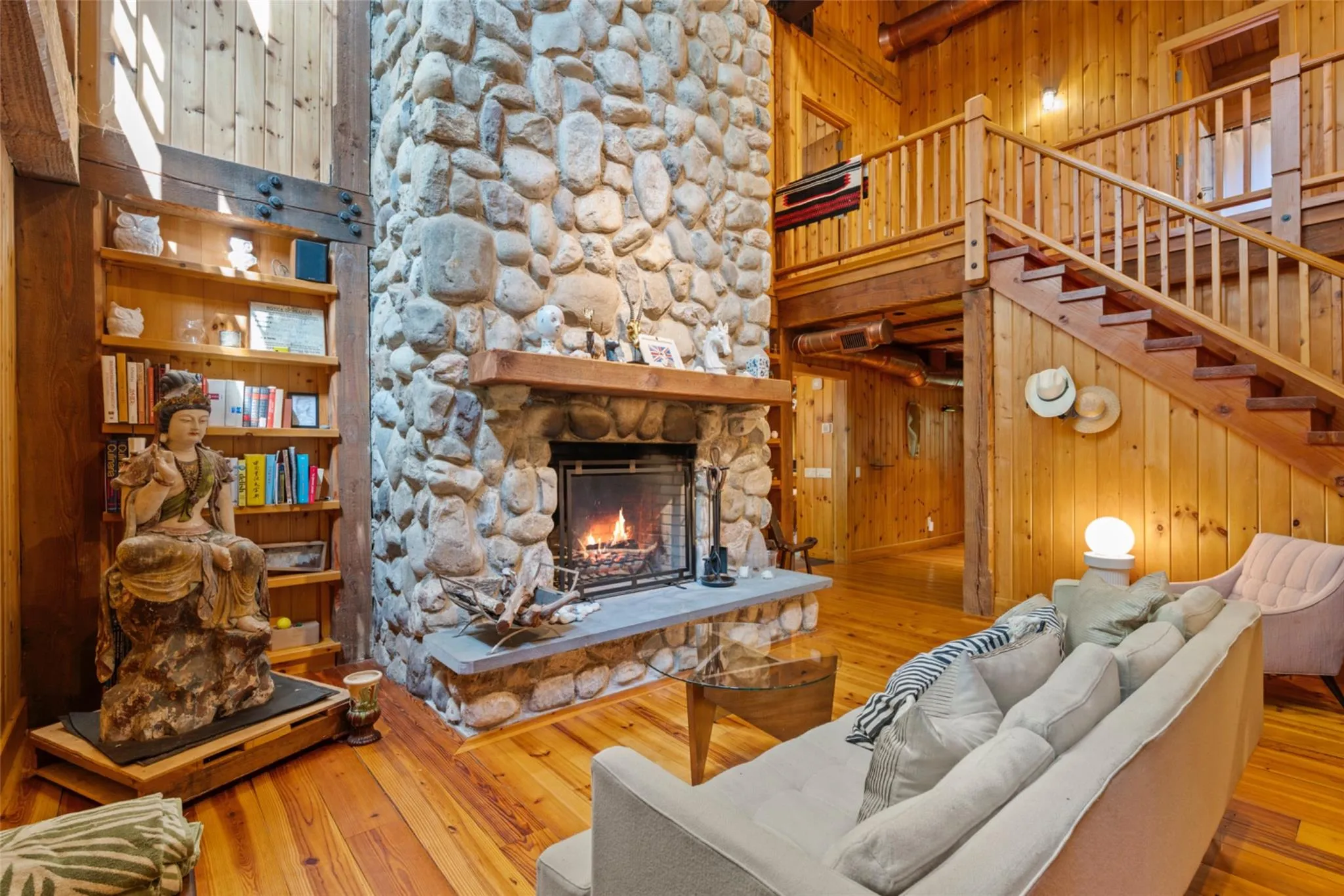Living room featuring wooden walls, wood-type flooring, a stone fireplace, stairway, and a towering ceiling Living room featuring wooden walls, wood-type flooring, a stone fireplace, stairway, and a towering ceiling