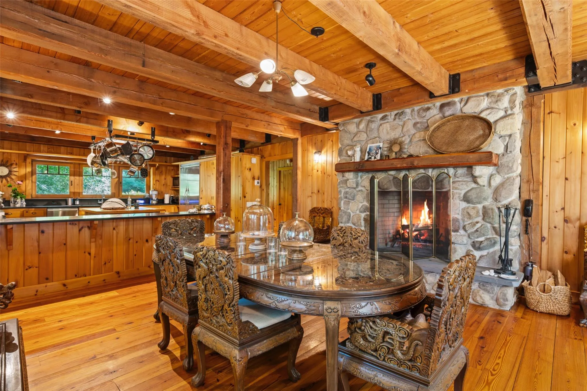 Dining area with light wood-type flooring, wood walls, wooden ceiling with exposed beams, and a stone fireplace Dining area with light wood-type flooring, wood walls, wooden ceiling with exposed beams, and a stone fireplace