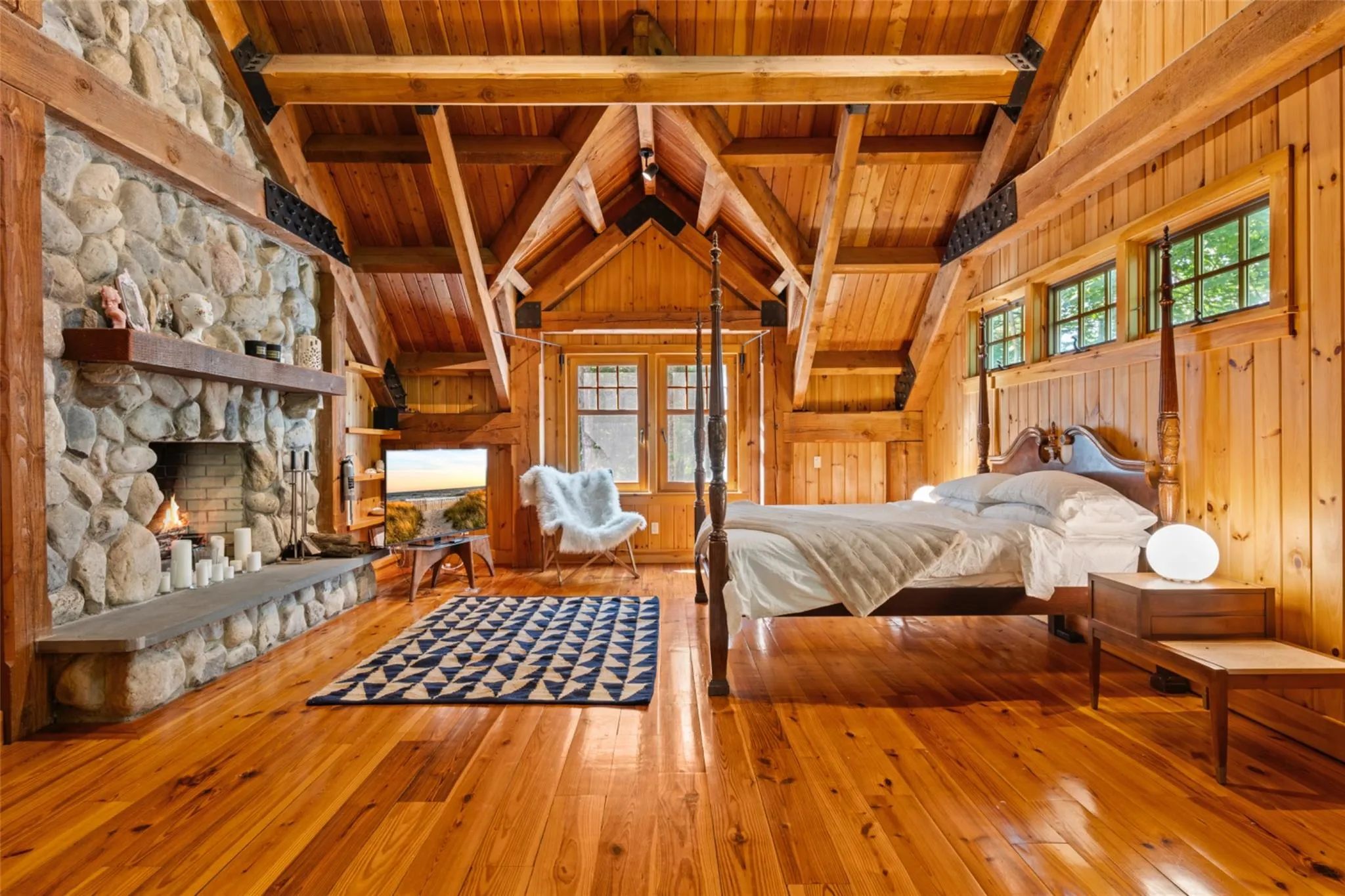Bedroom featuring wooden ceiling, wood walls, hardwood / wood-style flooring, multiple windows, and a fireplace Bedroom featuring wooden ceiling, wood walls, hardwood / wood-style flooring, multiple windows, and a fireplace