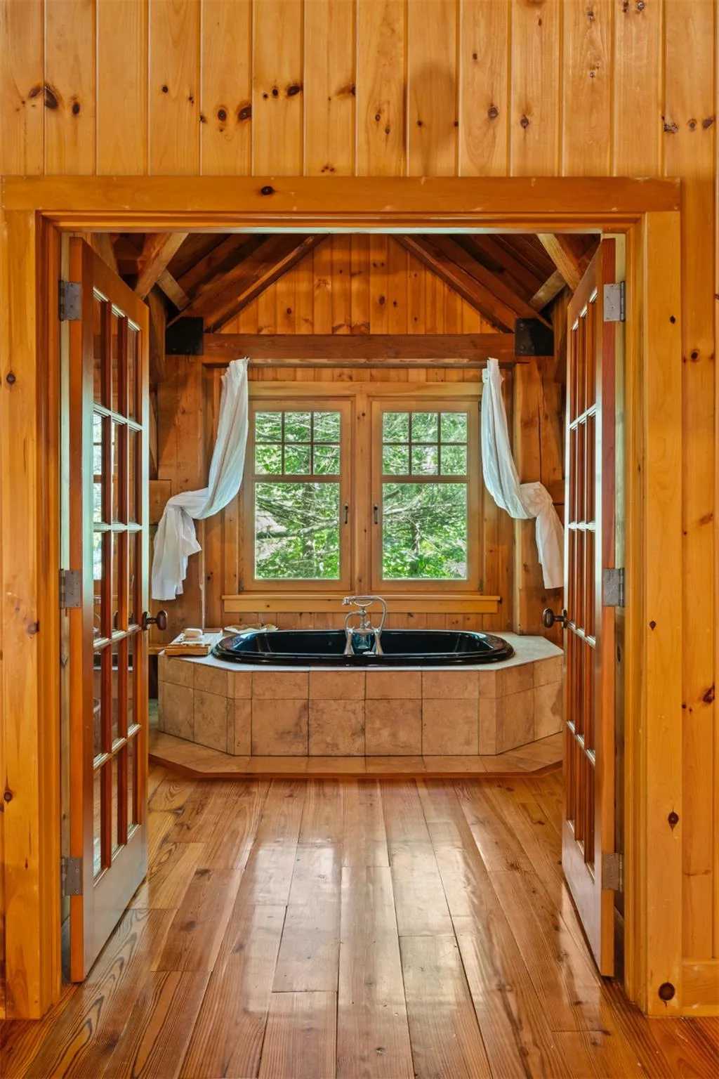 Bathroom with hardwood / wood-style floors, a garden tub, lofted ceiling, and wood walls Bathroom with hardwood / wood-style floors, a garden tub, lofted ceiling, and wood walls